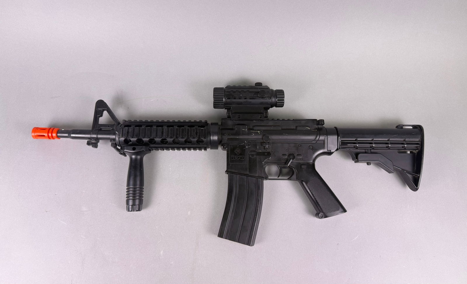 BBTac M83 Airsoft Electric Rifle: A BBTac M83 Airsoft Electric Rifle. This black plastic replica airsoft rifle is modeled after a modern M4/AR-15 style assault rifle, visibly distinguished by its bright orange barrel tip. It features