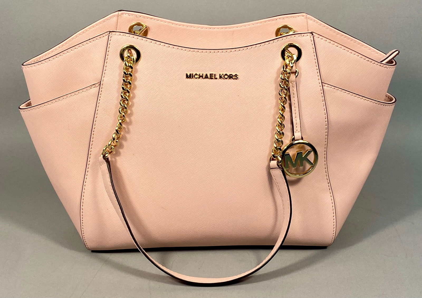 Michael Kors Jet Set Travel Large Blush Pink Saffiano Leather Shoulder Tote: A Michael Kors Jet Set Travel Large Shoulder Tote, crafted in blush pink Saffiano leather. This structured tote bag features gold-tone metal hardware and prominently displays "MICHAEL KORS" in gold le