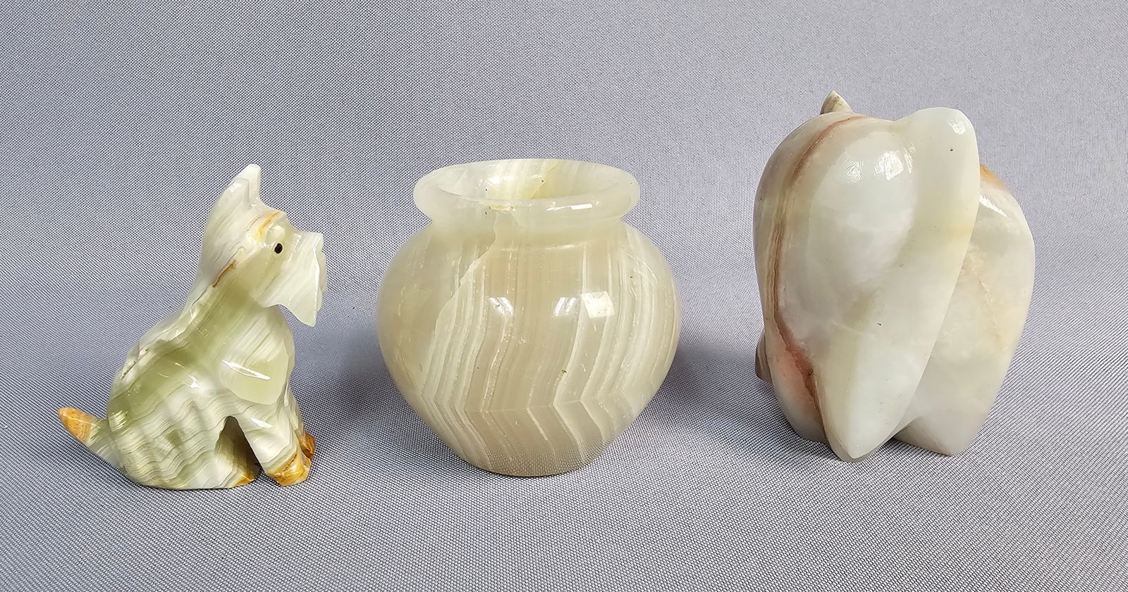Three Carved Onyx Decorative Objects: A collection of three carved onyx decorative objects, comprising a stylized terrier-type dog figurine with inset black eyes, a miniature globular vase, and a stylized elephant figurine. The dog and va