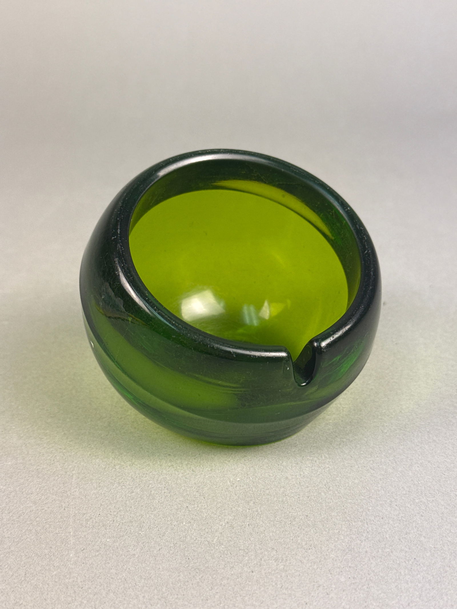 A Mid-Century Modern Viking Glass Green Orb Ashtray: A Mid-Century Modern Viking Glass green Orb ashtray. This heavy, translucent deep green glass ashtray features a spherical or globular body with a flattened base, and an angled, wide opening leading t