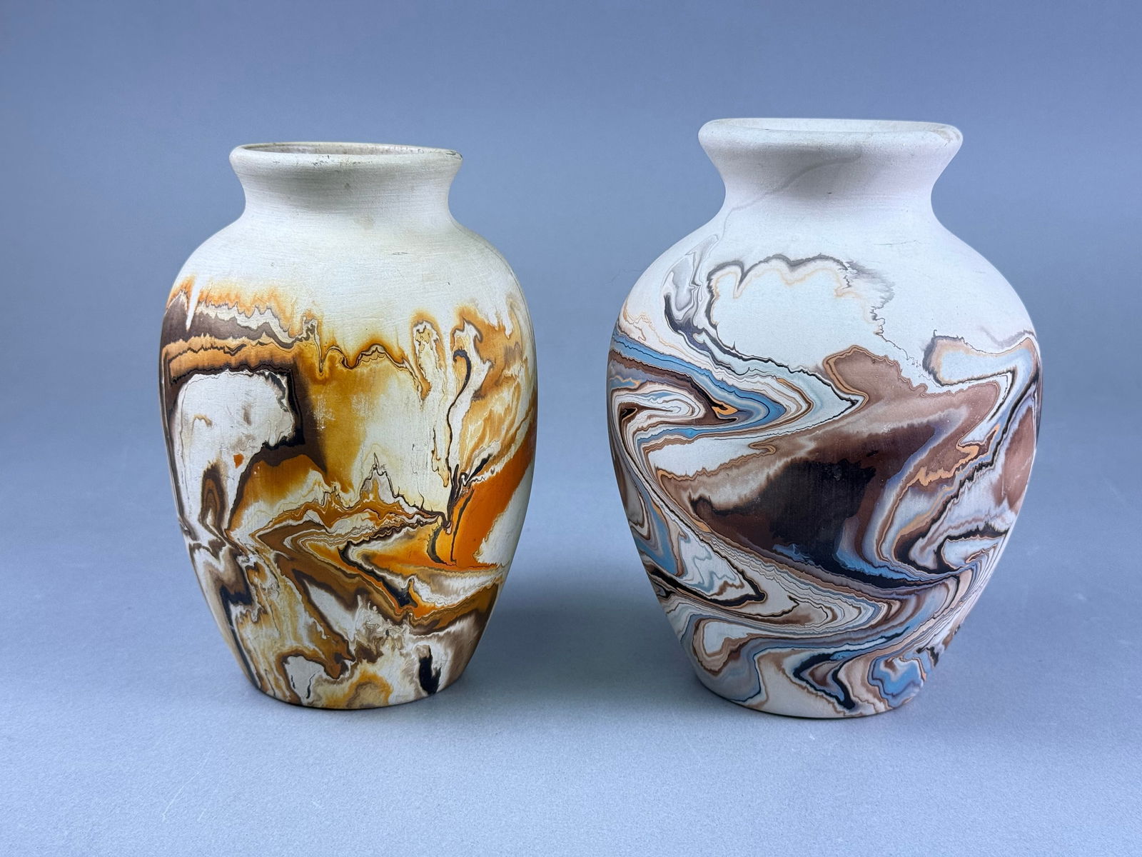 A Pair of Mid 20th Century Nemadji Pottery Swirled River Clay Vases: A pair of Nemadji Pottery swirled river clay vases, each featuring a distinctive marbled slip decoration. The vase on the left displays earth tones of brown, orange, and cream, while the vase on the r