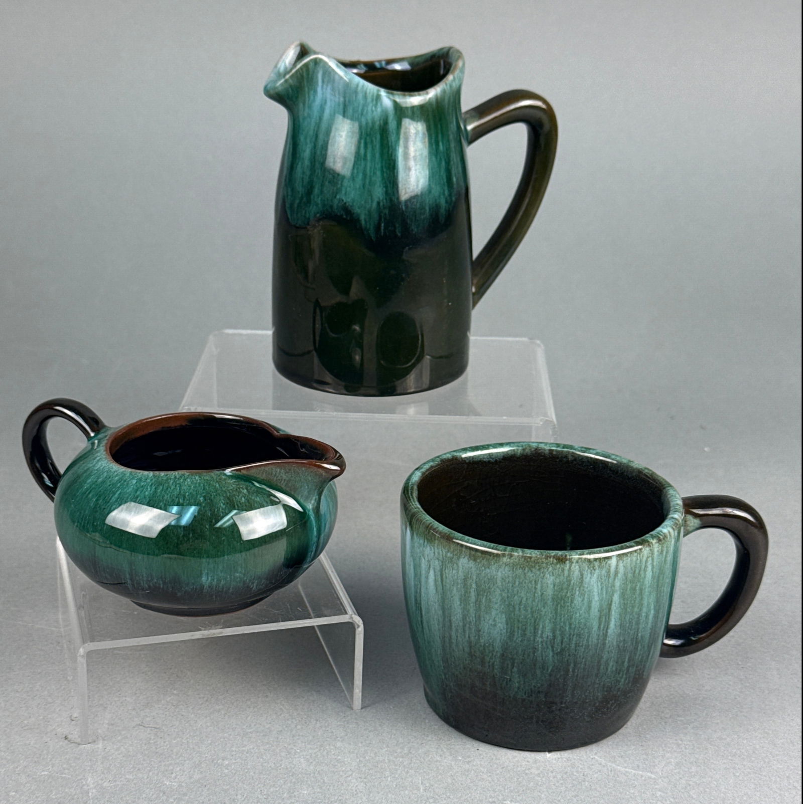 Three Blue Mountain Pottery Ceramic Creamers and Mug: A group of three ceramic vessels by Blue Mountain Pottery, Canada. Comprising a taller pitcher-style creamer, a wider, lower creamer, and a handled mug. Each piece features a distinctive flowing or dr