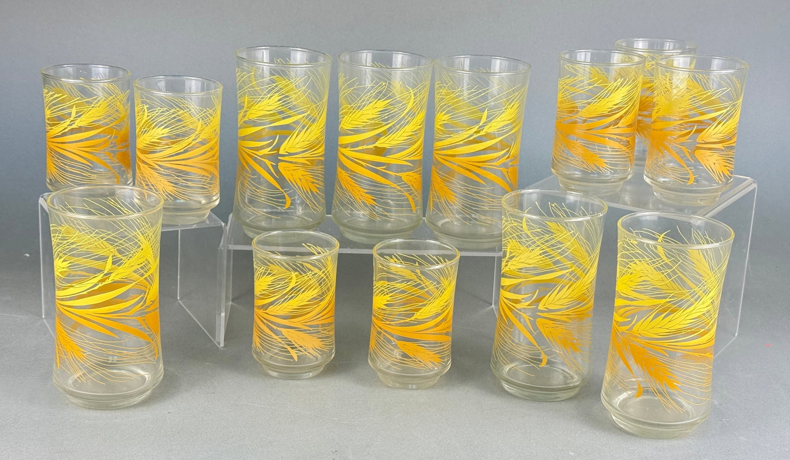 A Set of Fourteen Libbey 'Golden Wheat' Tumblers: A set of fourteen Libbey 'Golden Wheat' tumblers, comprising eight taller and six shorter glasses. Each clear glass tumbler features a two-tone yellow and orange stylized decorative pattern, suggestiv