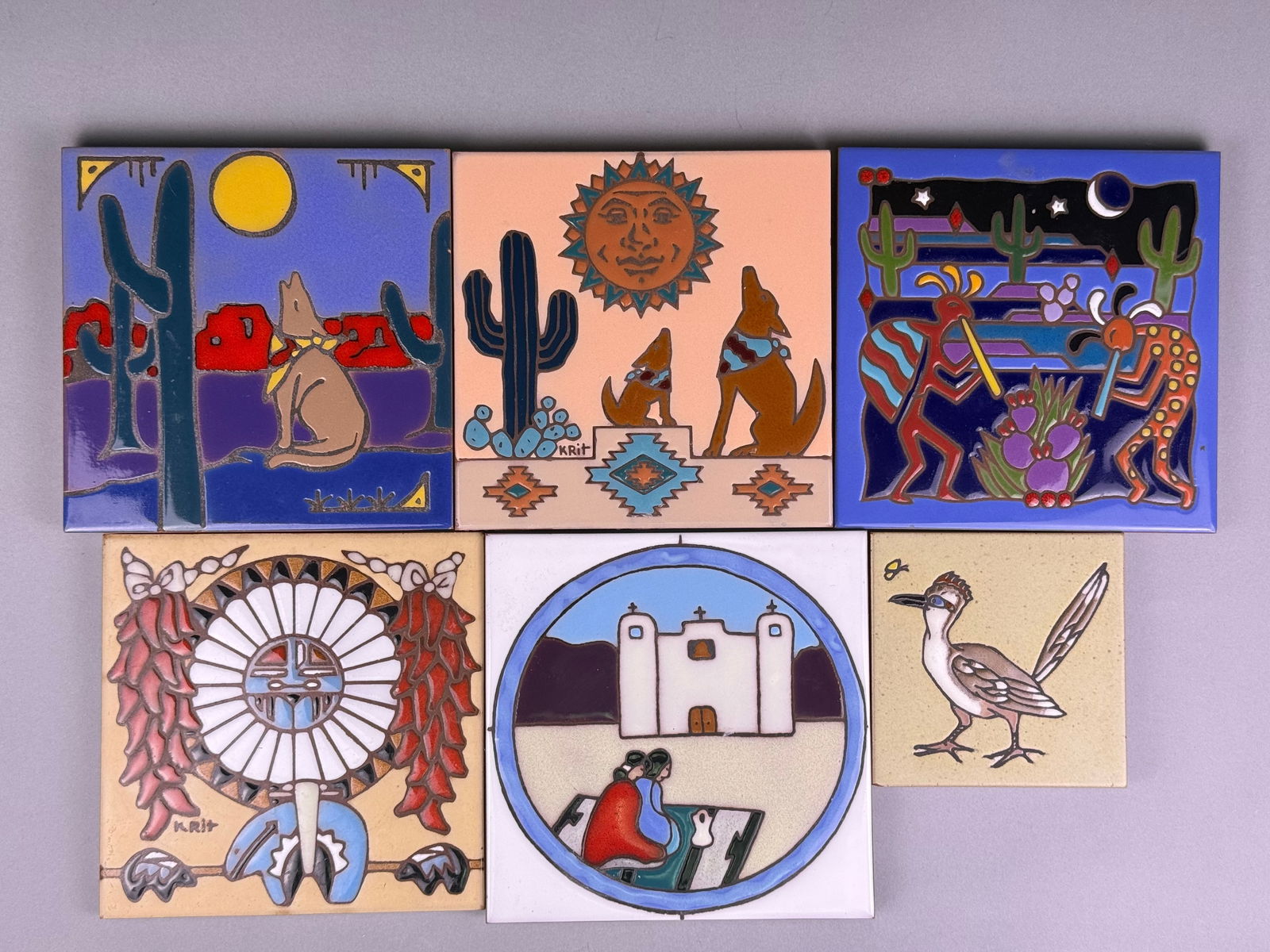 A Set of Six Southwestern-Inspired Glazed Ceramic Tiles: A set of six square glazed ceramic tiles, each depicting Southwestern or Native American-inspired folk art scenes. The designs feature desert landscapes with cacti, coyotes, a roadrunner, sun motifs,