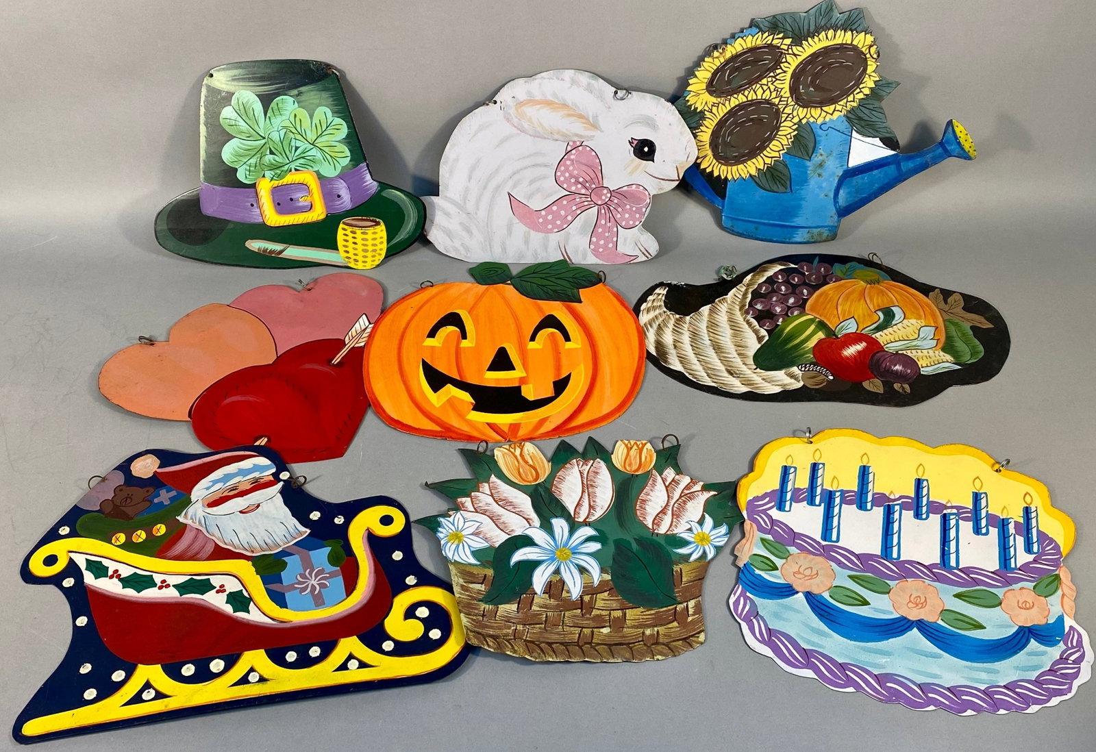 A Collection of Nine Folk Art Style Holiday and Seasonal Die-Cut Wall Hangings: A collection of nine decorative wall hangings, each crafted from a flat, cut-out heavy meatal, painted in a colorful folk art or country style. The collection depicts various holiday and seasonal them