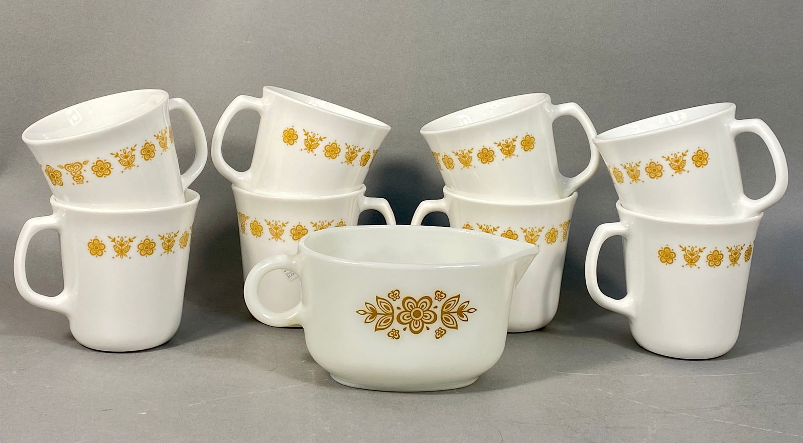 A Collection of Pyrex Butterfly Gold Mugs and Gravy Boat: A collection of eight opaque white glass mugs and one matching small pitcher/creamer by Pyrex and Corning, adorned with the 'Butterfly Gold' pattern. This mid-20th century aesthetic features a vibrant