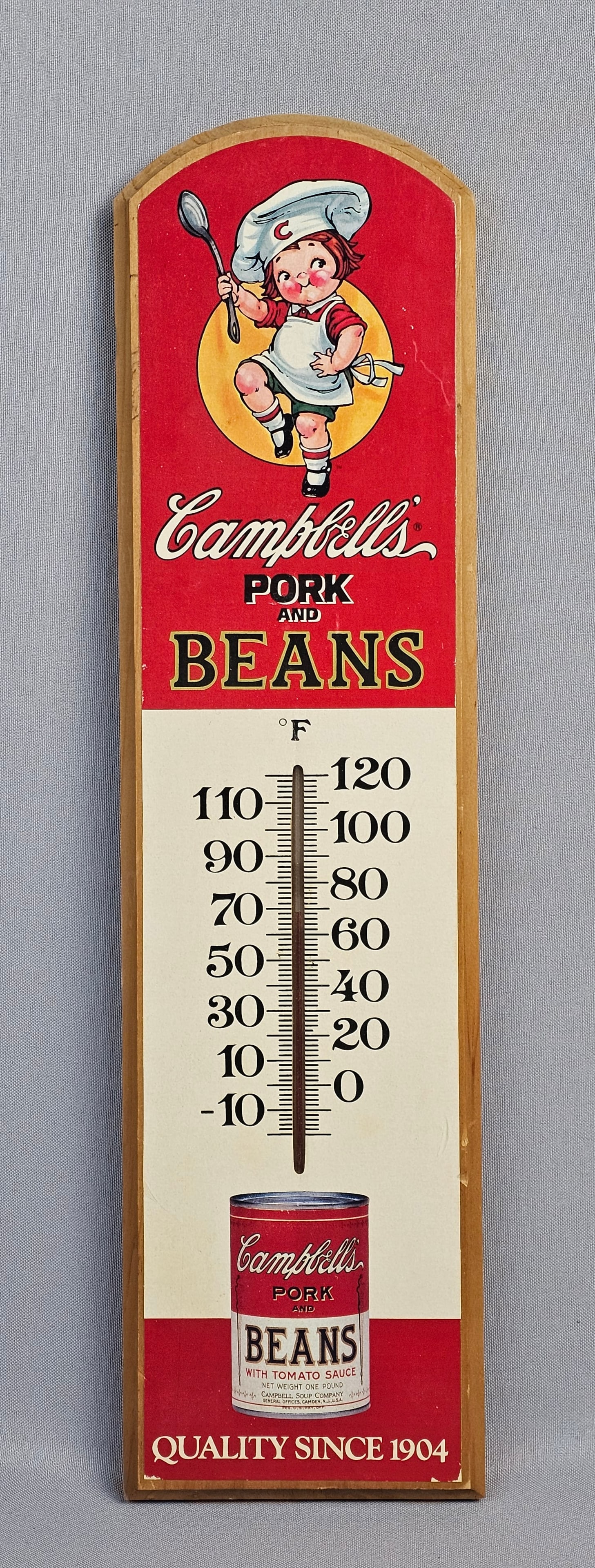 A 1987 Campbell's Pork and Beans Advertising Thermometer: A vintage Campbell's Pork and Beans advertising thermometer, featuring a wooden backing with a printed face. Approximately 17 inches tall The item is in good apparent condition. Minor wear is present 