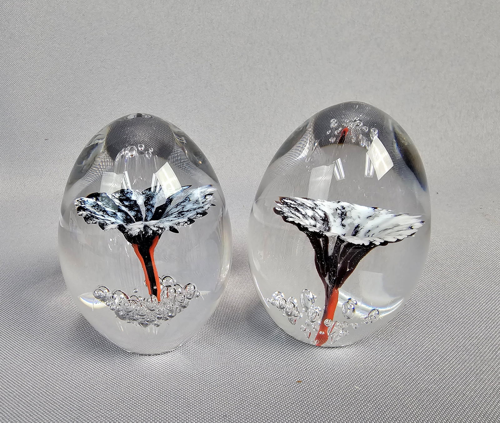 A Pair of Daum France Signed Art Glass Egg Shape Paperweights: A pair of Daum France signed art glass egg shape paperweights. Each is an ovoid form of clear glass, encapsulating an internal lampwork or fused glass sculpture featuring a stylized black and white or