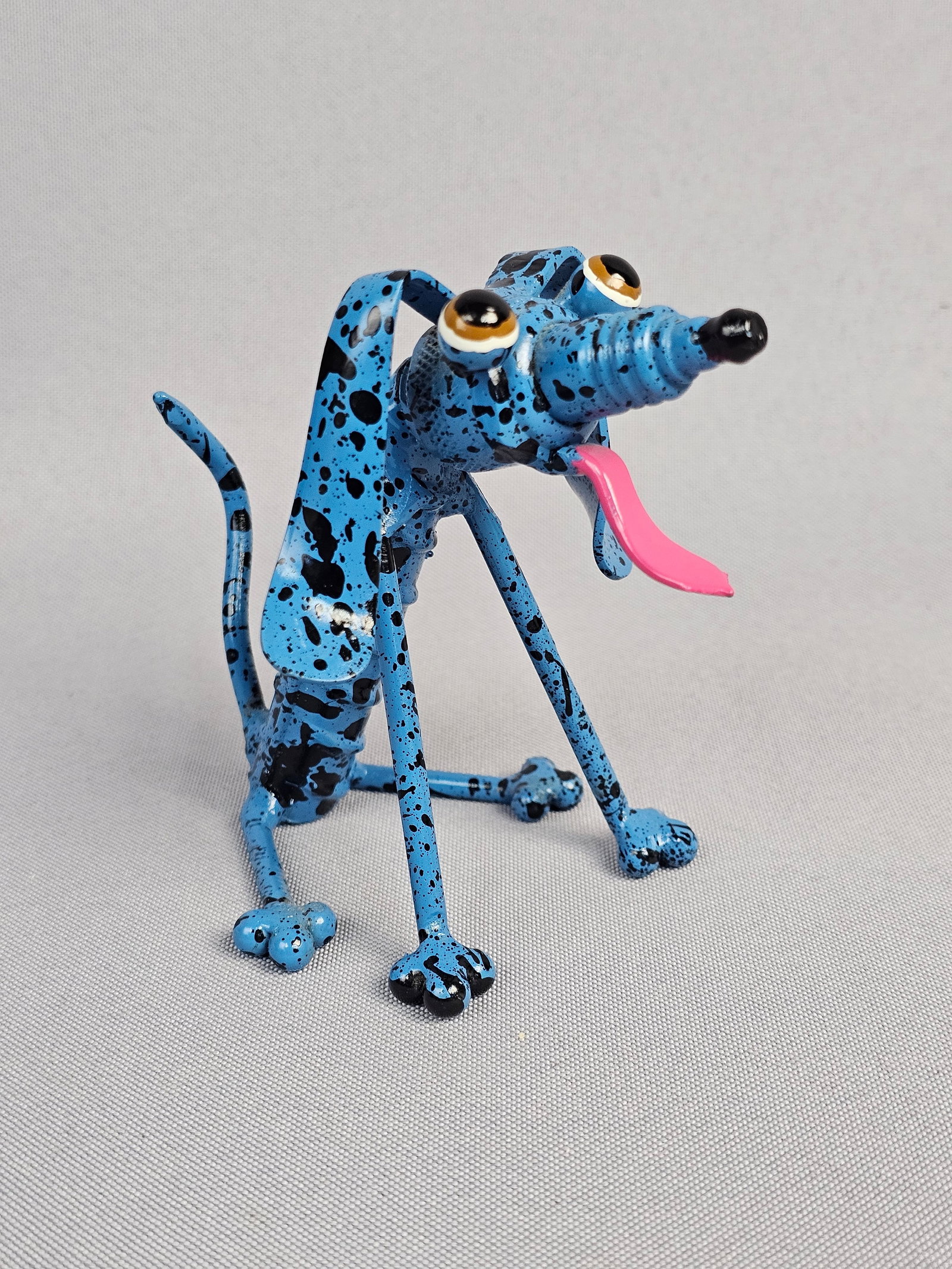 A Whimsical Folk Art Style Welded Metal Sculpture of a Sitting Dog: A whimsical folk art style sculpture depicting a sitting dog, constructed from welded and bent metal components, painted in a speckled bright blue with black spots. A capital white letter "P"