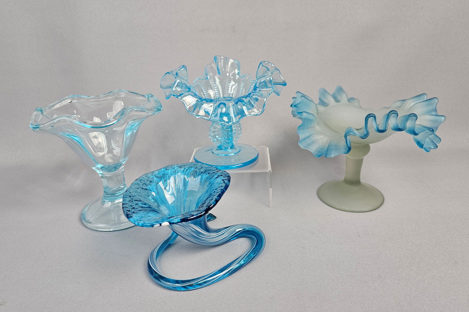 A Group of Four Blue Glass Compotes and Decorative Objects: All pieces measure between 3 and 5 inches tall. All pieces appear in good overall condition. Small chip on ruffled rim of one compote.