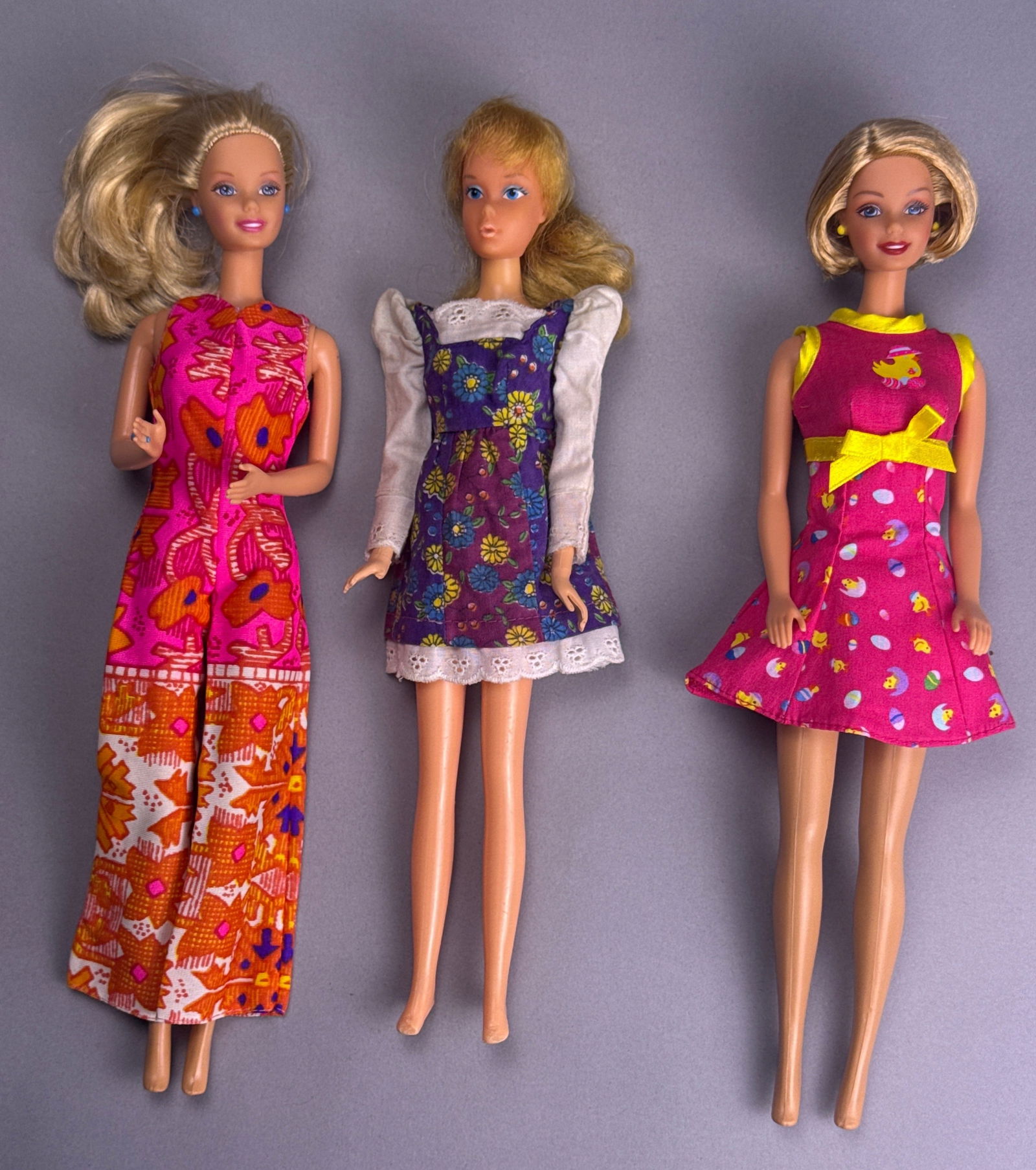 Three Vintage Barbie Dolls by Mattel, 1960s-1970s: This lot features three vintage Barbie dolls by Mattel, made primarily of plastic with fabric clothing. The leftmost doll, marked '© 1976 MATTEL INC.' on its lower back, is dressed in a vibrant p
