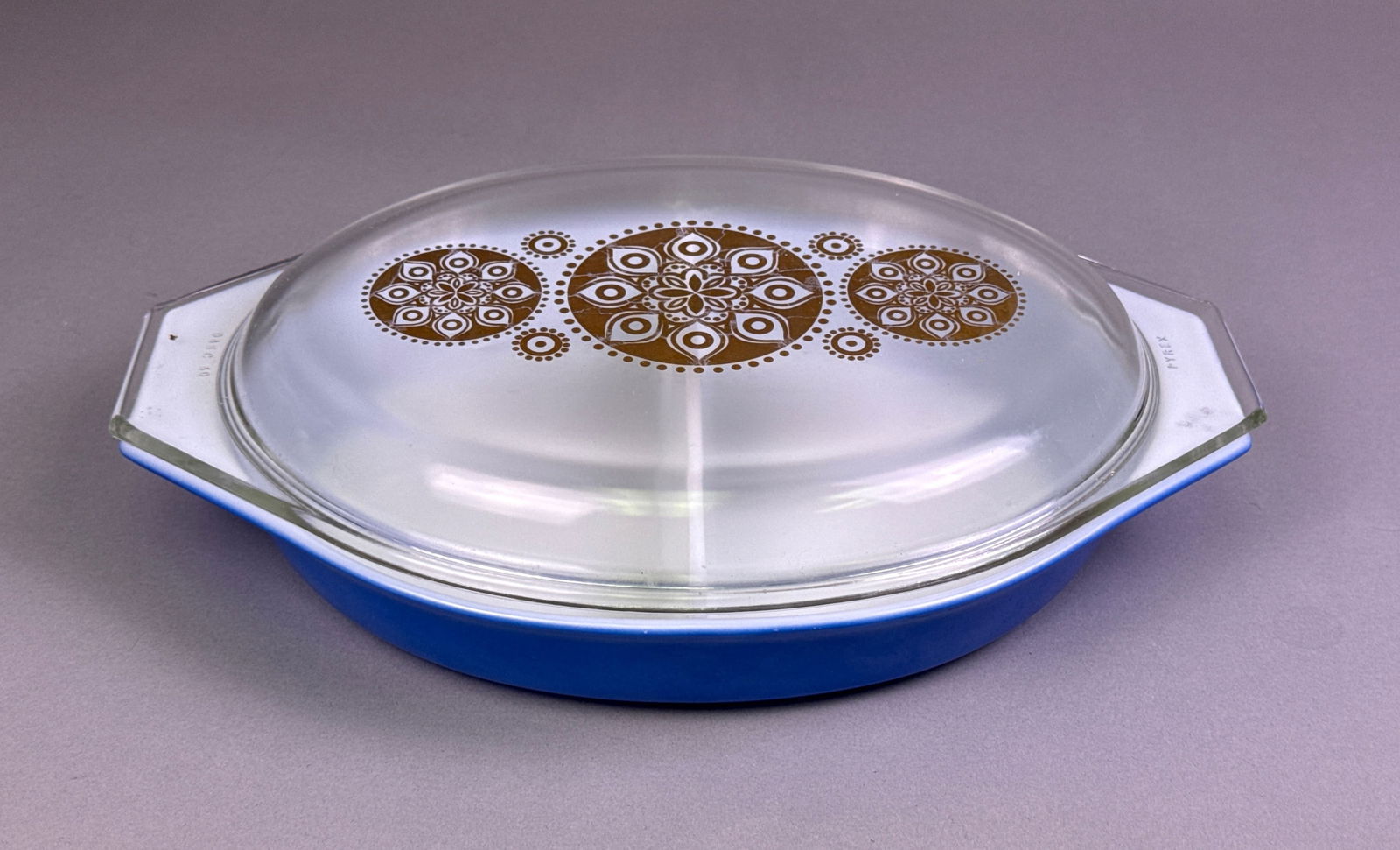 Pyrex Royal Blue Oval Divided Casserole Dish with Gold Medallion Lid, 1961 Promo: A vintage Pyrex Royal Blue Oval Divided Casserole Dish with Gold Medallion Lid, identified as a 1961 promotional item. This 1 1/2 quart opaque glass base features a vibrant blue exterior and a white i