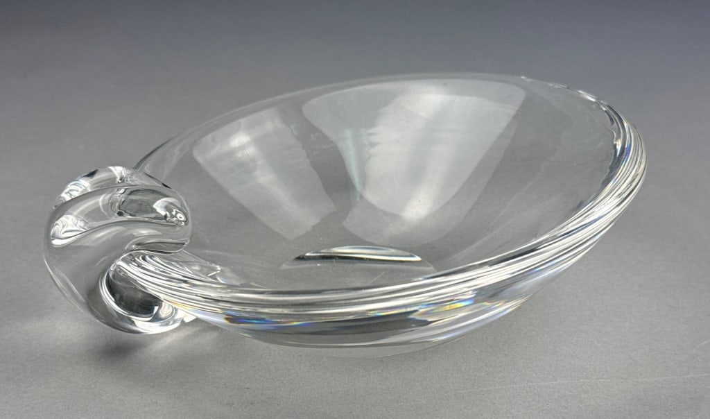 Steuben Crystal Glass Sloping Bowl Ashtray: A Steuben crystal glass sloping bowl ashtray. This clear colorless glass object features an elongated oval form with a sculptural, C-scroll handle-like extension on one side, presenting a modernist, o