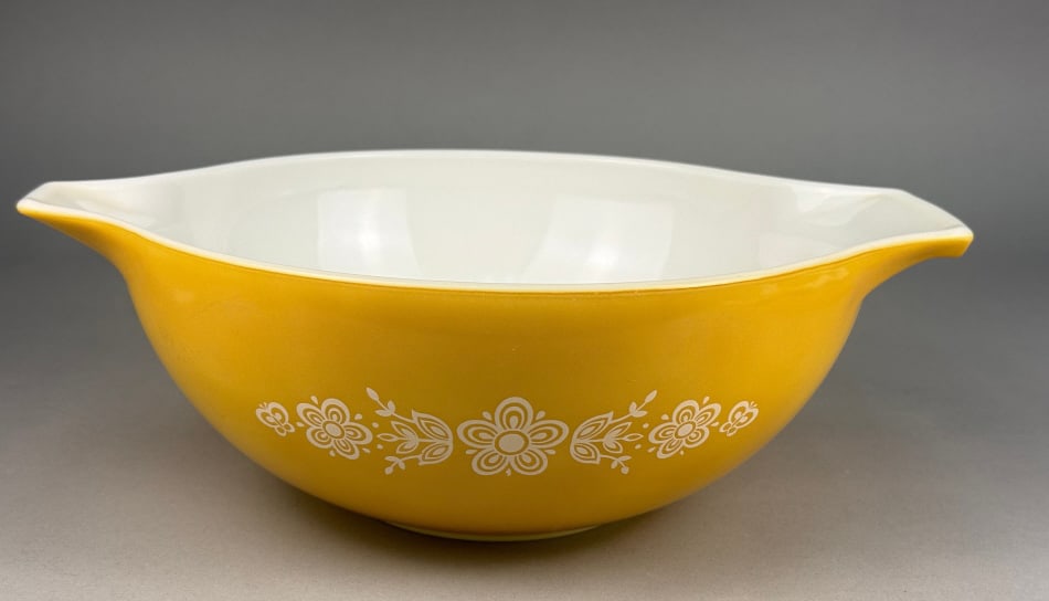 Pyrex Butterfly Gold Cinderella Nesting Mixing Bow: A Pyrex 'Butterfly Gold' pattern Cinderella nesting mixing bowl, model 443. This round opalescent glass bowl features a yellow exterior with a white interior. It is designed with two extended 'ears' o