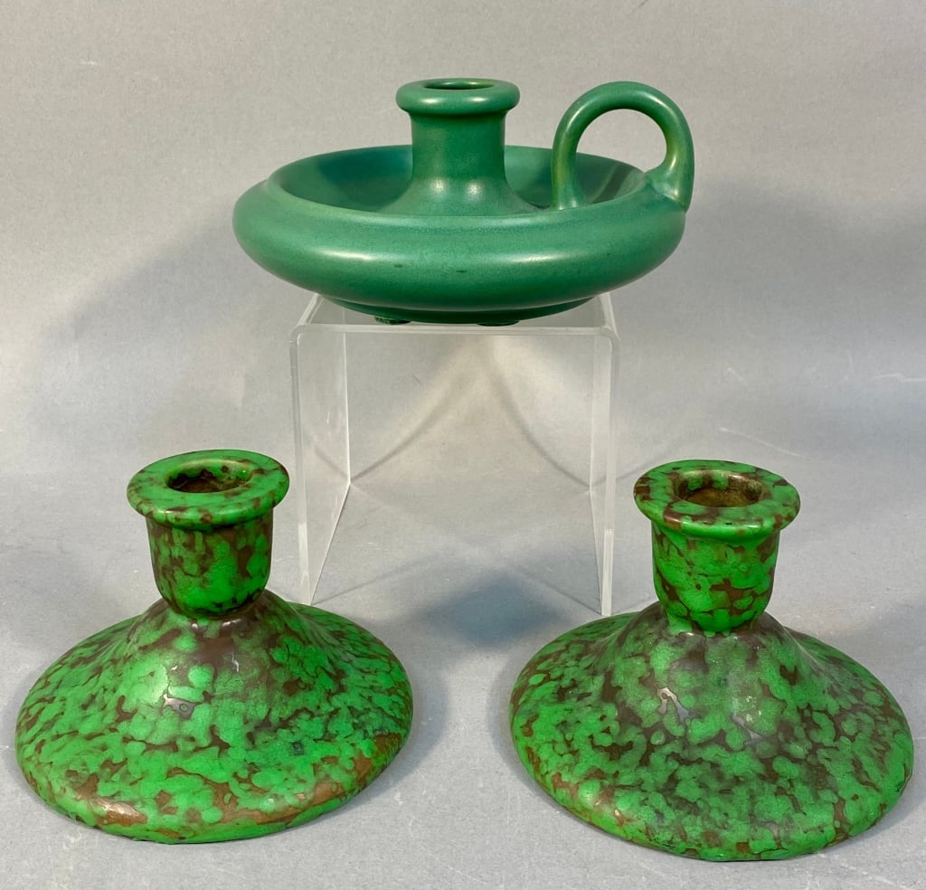 A Green Glazed Ceramic Chamberstick and a Pair of: This lot comprises three ceramic candle holders. The single chamberstick features a smooth, matte, uniform green glaze over a simple, rounded form with a shallow drip pan and a loop handle. Its unders