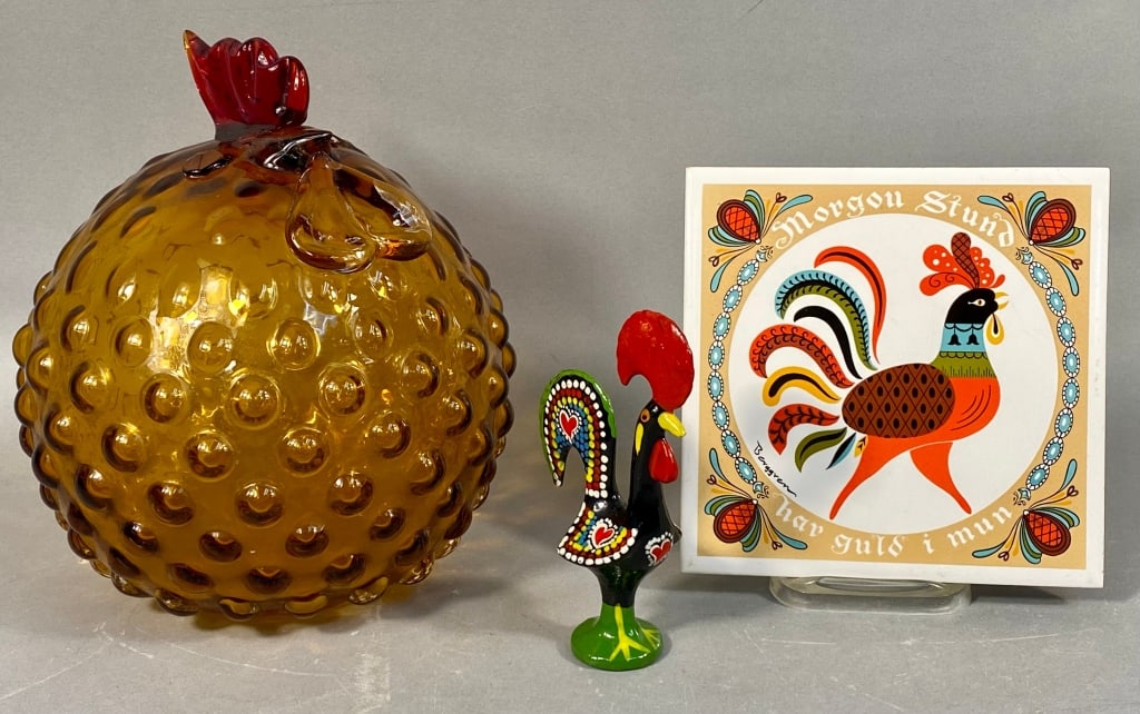 A Group of Three Rooster-Themed Decorative Objects: A 1970s hand blown amber hobnail glass rooster, featuring a globular body with a textured hobnail surface, a stylized red glass crest, and clear glass wattle. Accompanying this is a smaller folk art-s