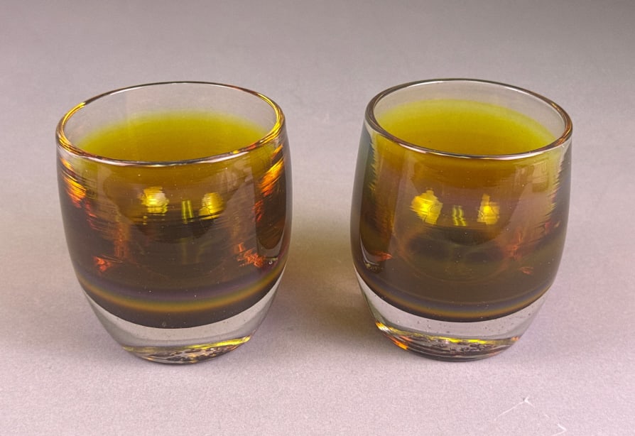 Glassy Baby Candle Votive Holders: Each votive features a distinctive color gradient, transitioning from a clear, thick base through a smoky amber-brown mid-section with iridescent highlights, to a yellowish-green at the rim. The heavy
