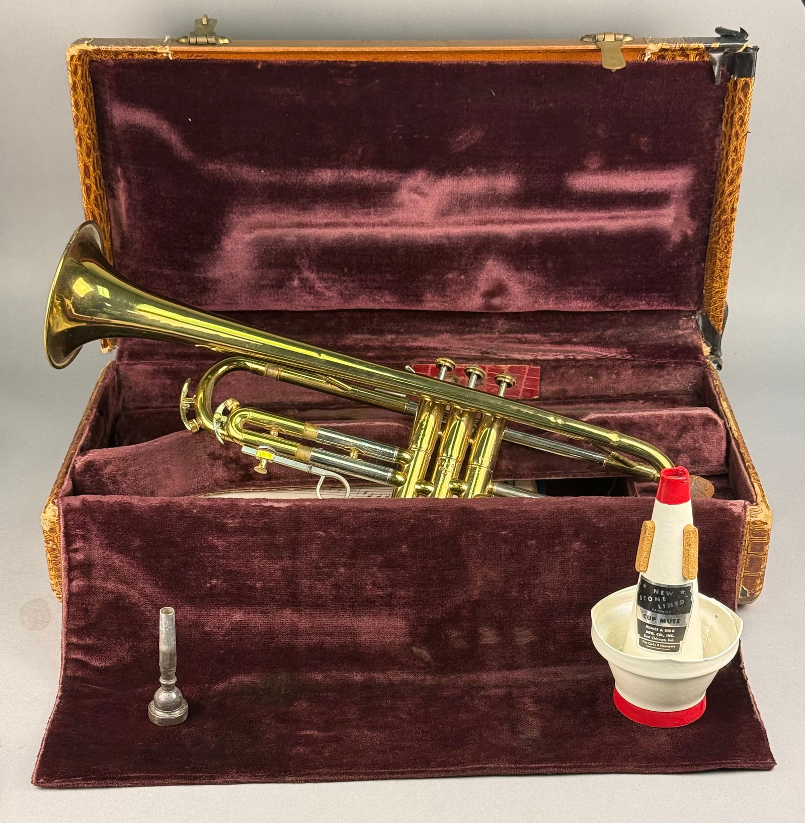 Reynolds Brass Trumpet with Accessories and Vintage Case: A collection of nine items centered around a brass trumpet with a golden lacquer finish and nickel/silver trim on the slides. The trumpet bell is engraved with the maker's name "Reynolds" an