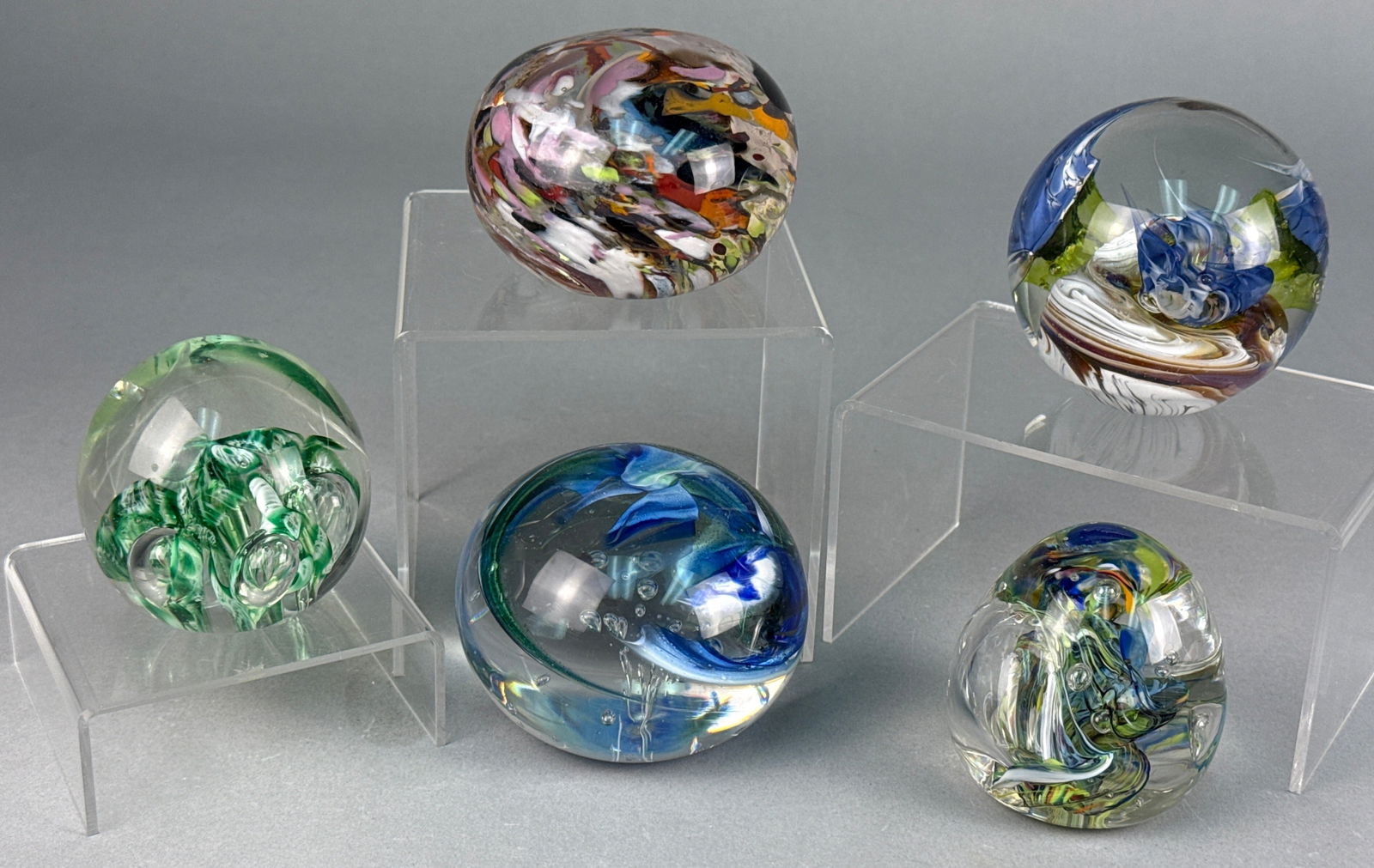 A Group of Five Contemporary Art Glass Paperweights: A group of five art glass paperweights, comprising three spherical and two ovoid forms. Each piece is crafted from clear glass encapsulating vibrant, abstract internal designs featuring varied swirlin