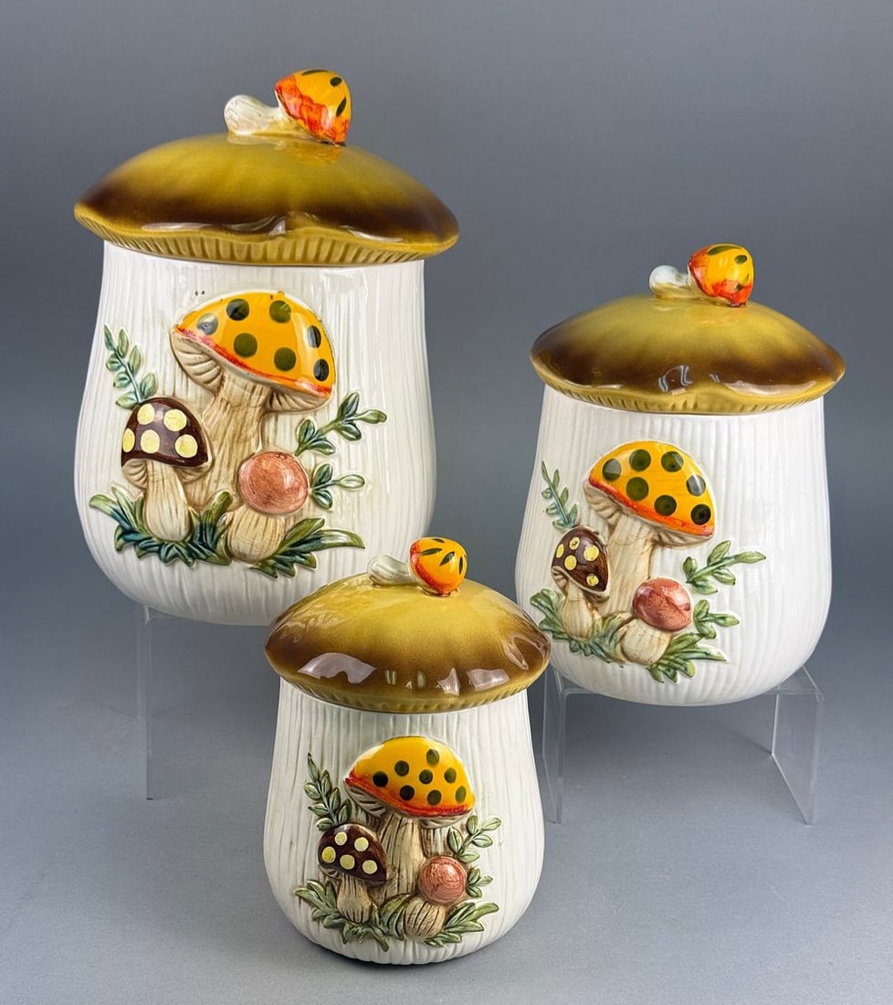 Three Sears Merry Mushroom Graduated Ceramic Canisters, 1983: A set of three 'Merry Mushroom' ceramic canisters by Sears, Roebuck and Co. Each graduated canister features a ribbed white cylindrical body, relief-molded and painted with mushroom clusters and green