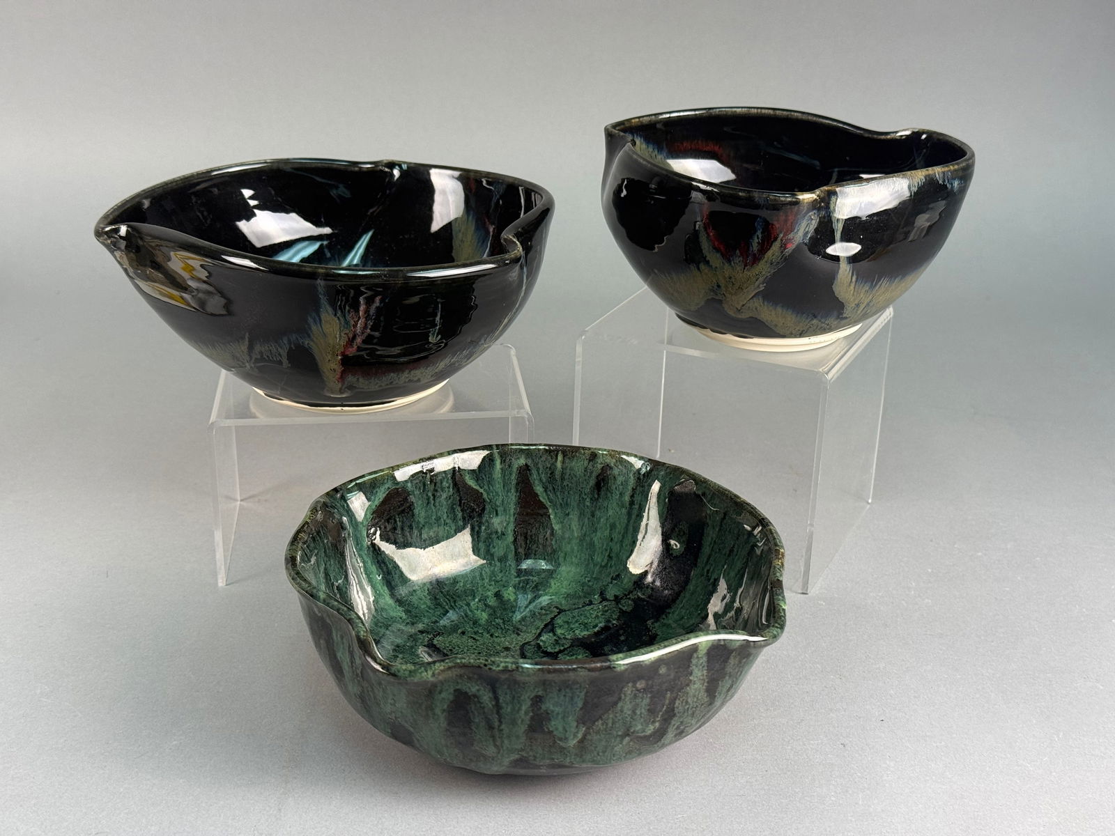 Three Studio Pottery Bowls by Joan Wageman and Bonnie Klein: A group of three studio pottery bowls, one by Joan Wageman and two by Bonnie Klein. Each bowl presents an organic, free-form shape with an undulating rim. Two bowls feature a high-gloss black glaze ad