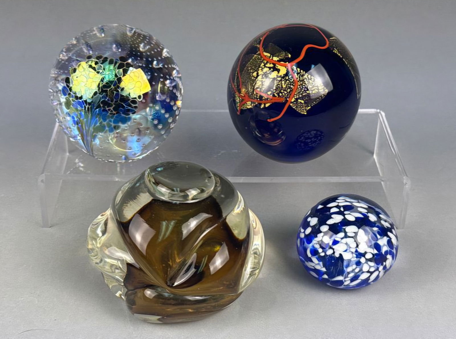 A Collection of Modern Art Glass Paperweights and Sculpture: A collection of four distinct glass objects, comprising two signed spherical paperweights, one abstract sculptural form, and one smaller spherical paperweight. The first spherical paperweight is craft
