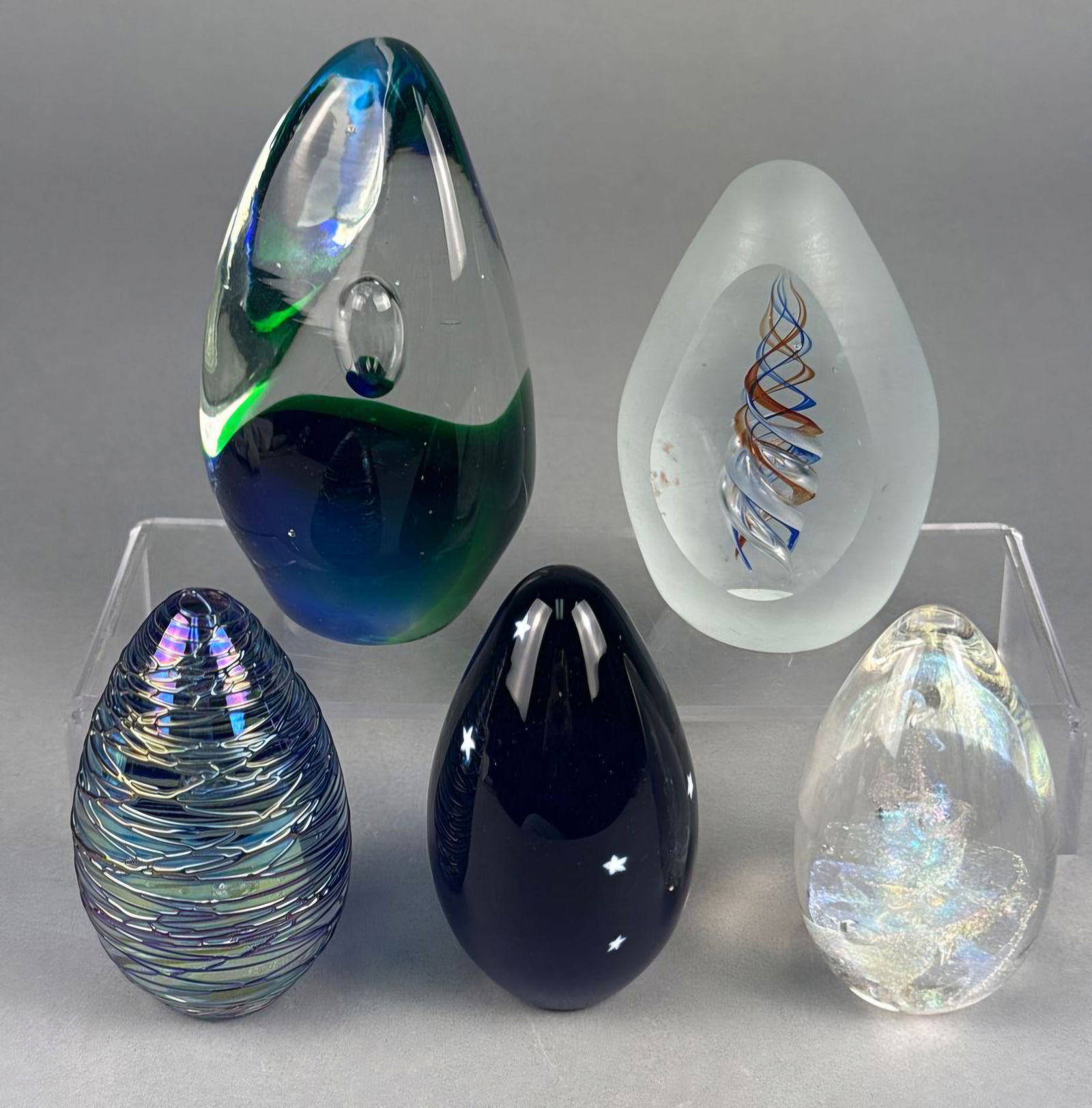 A Collection of Art Glass Egg-Shaped and Controlled Bubble Paperweights: A collection of five decorative glass objects, primarily ovoid or egg-shaped, functioning as paperweights. The collection includes a large clear glass piece with internal teal and blue coloration tran
