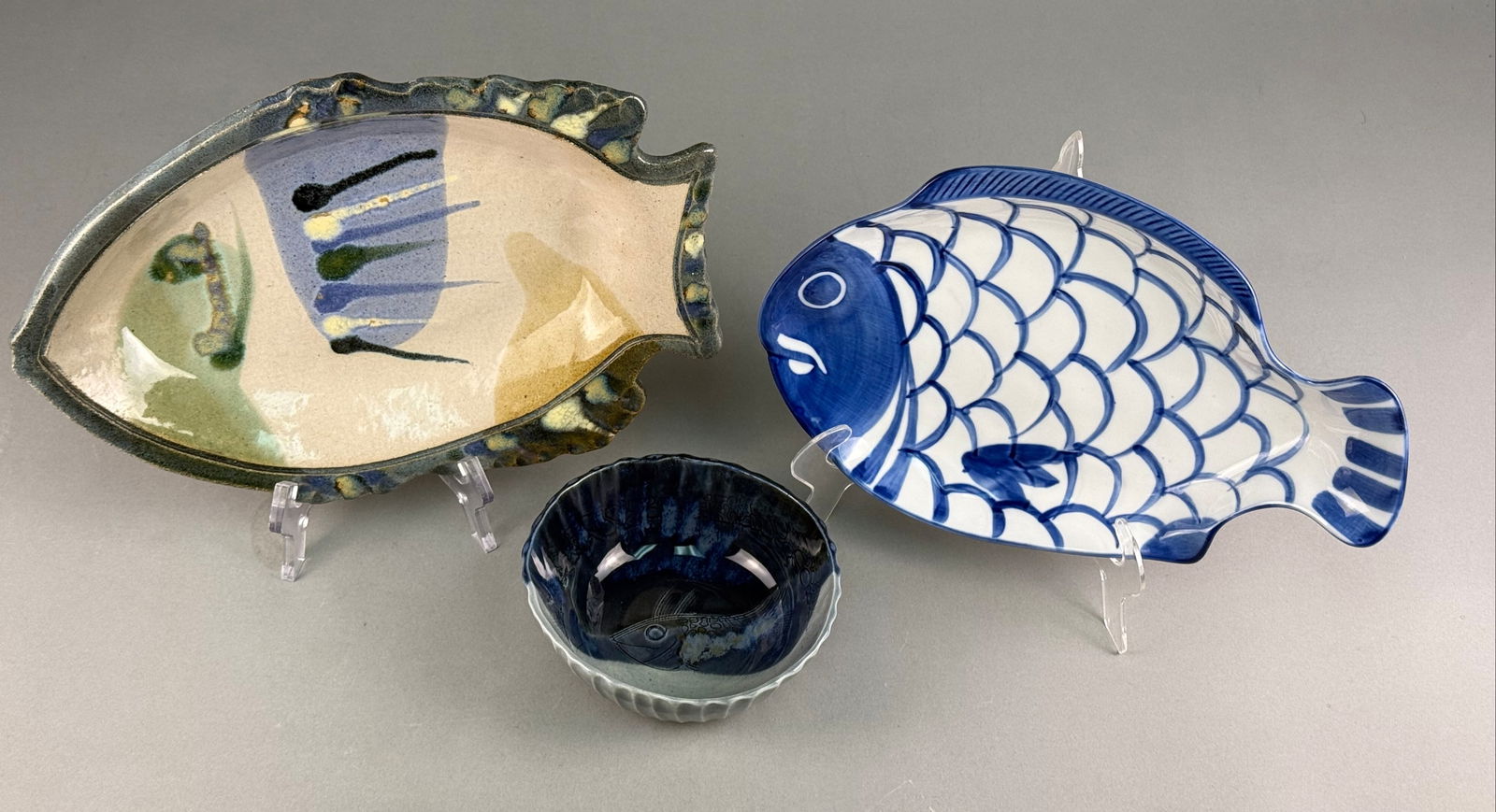 A Trio of Studio and Designer Ceramic Fish Tableware: A collection of three pieces of ceramic tableware, all featuring fish motifs. The lot includes two fish-shaped platters and one small bowl. The first item is a handmade studio pottery fish platter wit