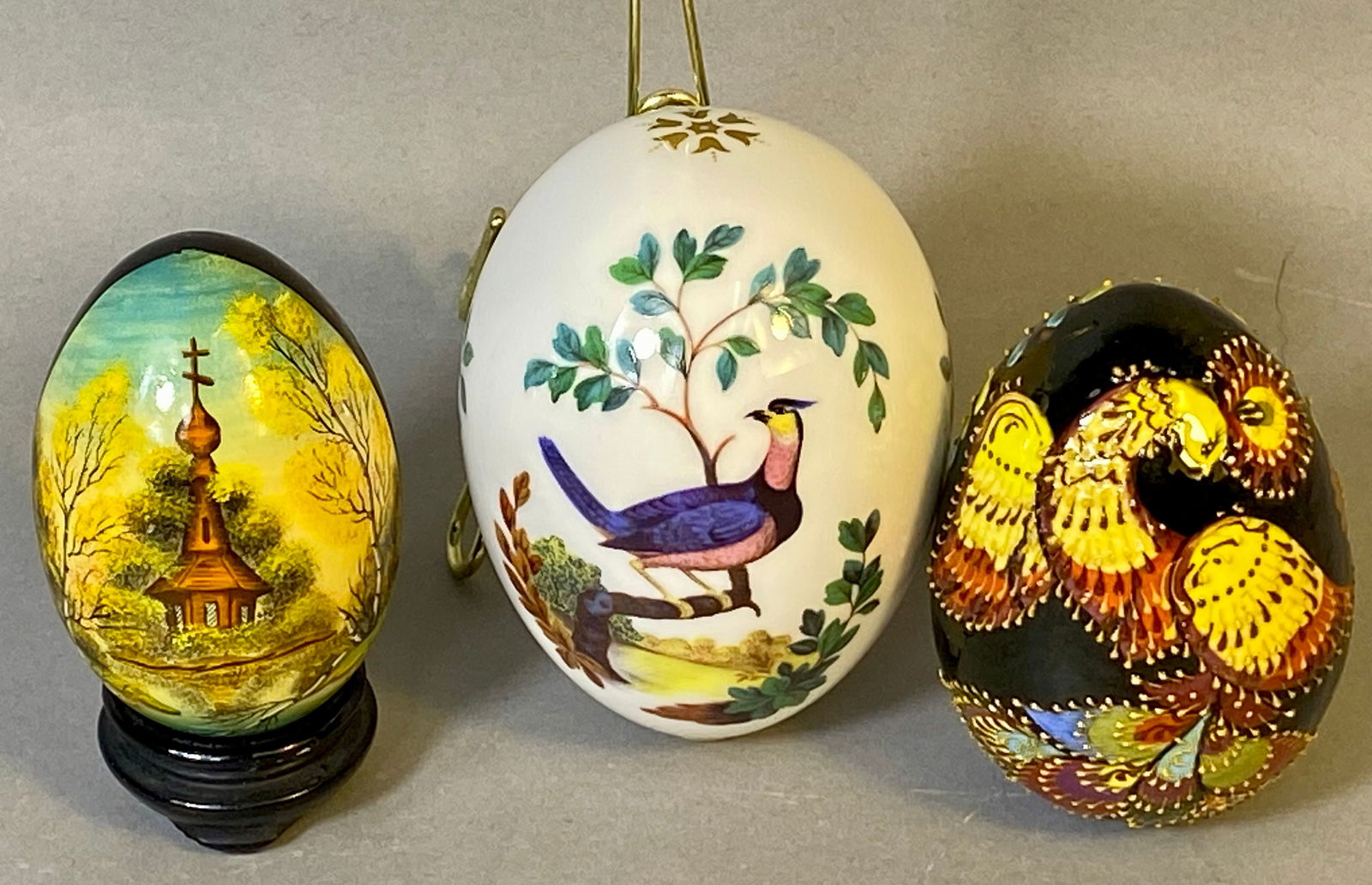A Trio of Decorative Eggs including Minton Fine Bone China Bird Egg: A collection of three decorative egg ornaments. The central item is a Minton fine bone china hanging egg ornament, finished in white glaze with gilt accents. The decoration features a transfer-printed