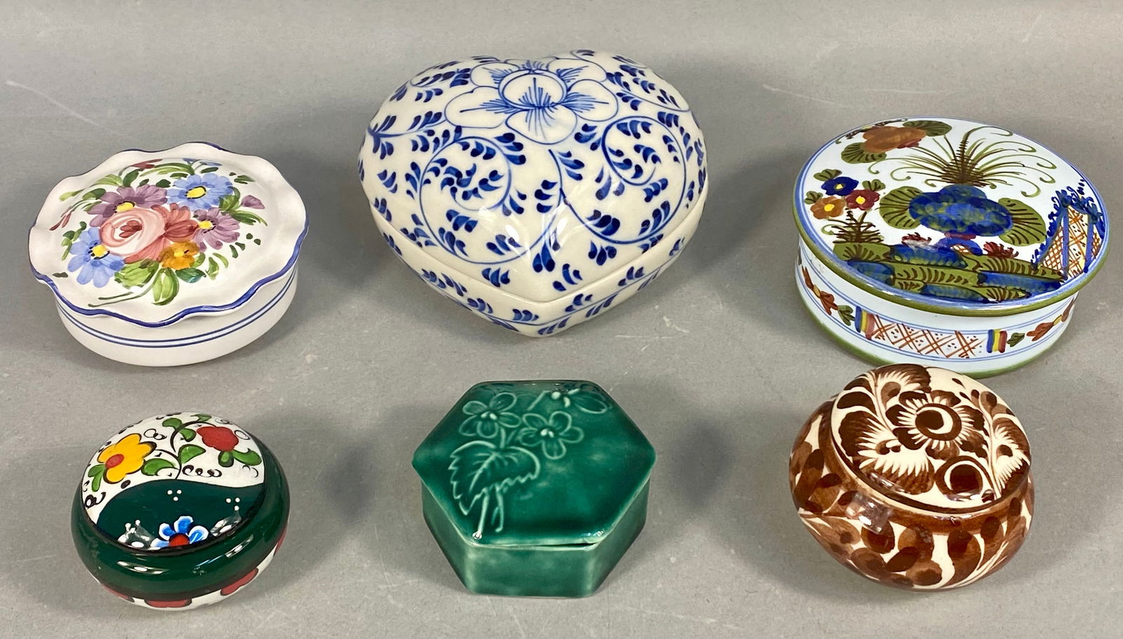 A Collection of 6 Glazed Ceramic and Porcelain Lidded Trinket Boxes: A collection of six glazed ceramic and porcelain lidded trinket boxes, exhibiting diverse contemporary decorative techniques and regional styles. The collection includes a heart-shaped porcelain box d