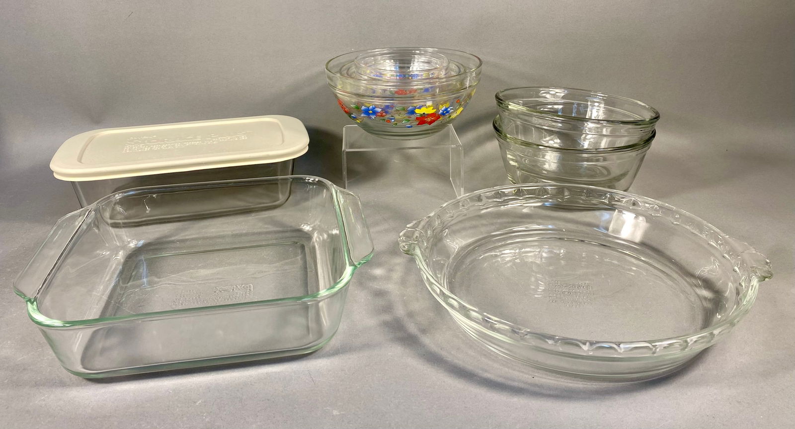 A Collection of 11 Pyrex and Anchor Hocking Clear Glass Baking and Storage Kitchenware: A collection of 11 pieces of clear heat-resistant glass kitchenware, primarily manufactured by Pyrex and Anchor Hocking. The lot includes six clear glass mixing bowls decorated with a multicolor flora