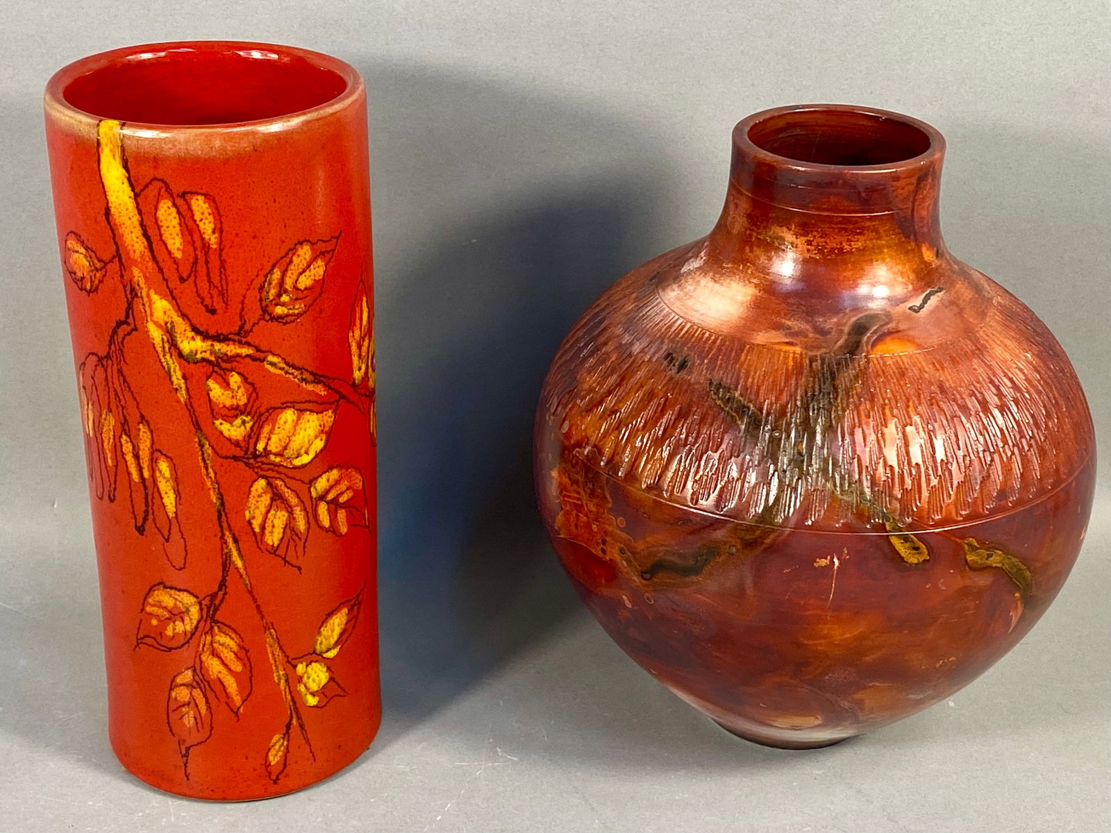 Two Mid-Century Modern Ceramic Vases, one Raymor 1979 and one signed A. Serra: A collection of two Mid-Century Modern ceramic art vases. The first vase is a tall cylindrical form with a matte orange-red ground. The decoration features a stylized branch with yellow-orange leaves
