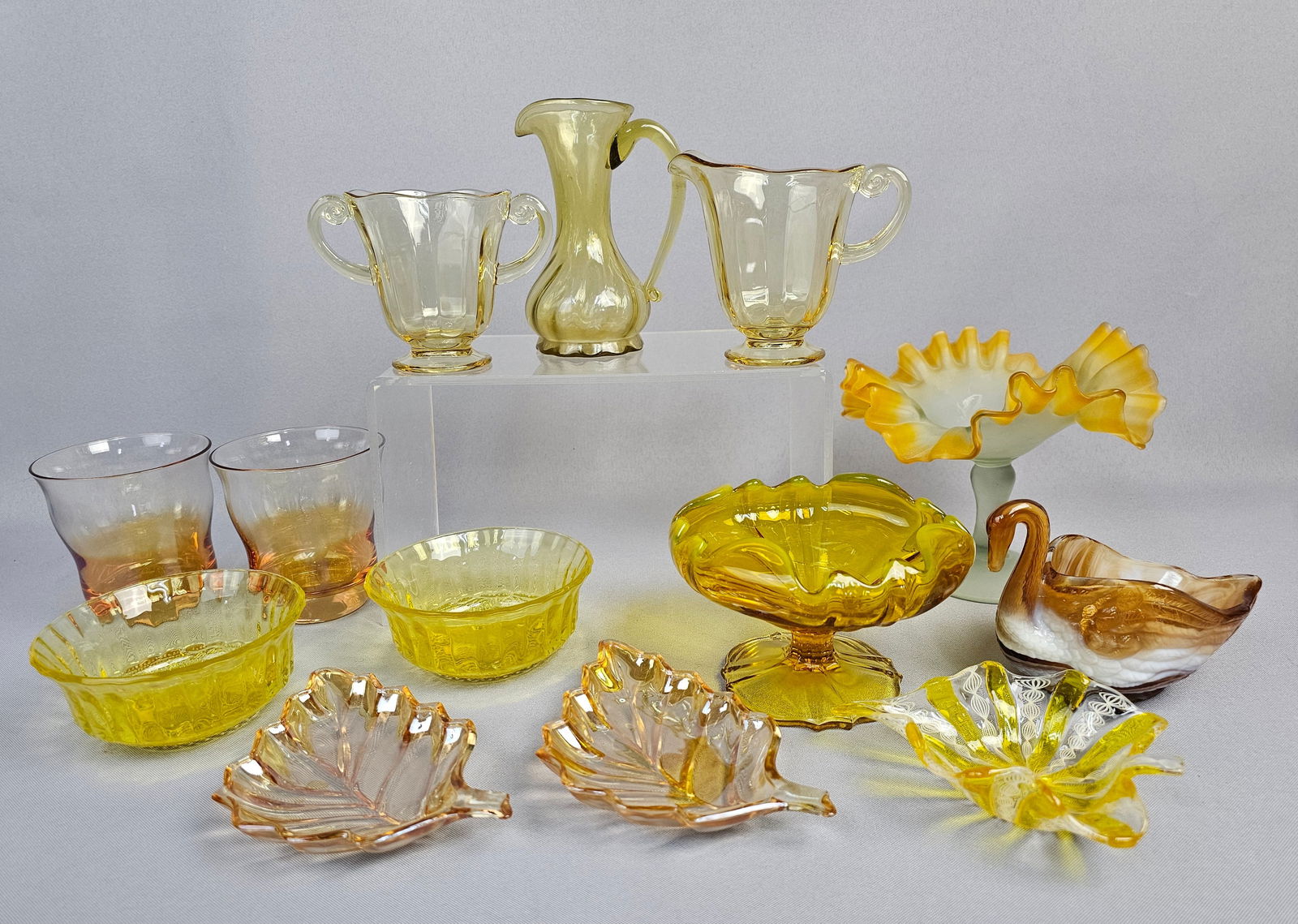 A Collection of Vintage and Antique Yellow, Amber, and Peach Glass Tableware and Decorative Items: A large collection of glass tableware and decorative items, predominantly in hues of yellow, amber, and peach, with some pieces incorporating white or frosted glass. The collection includes a creamer