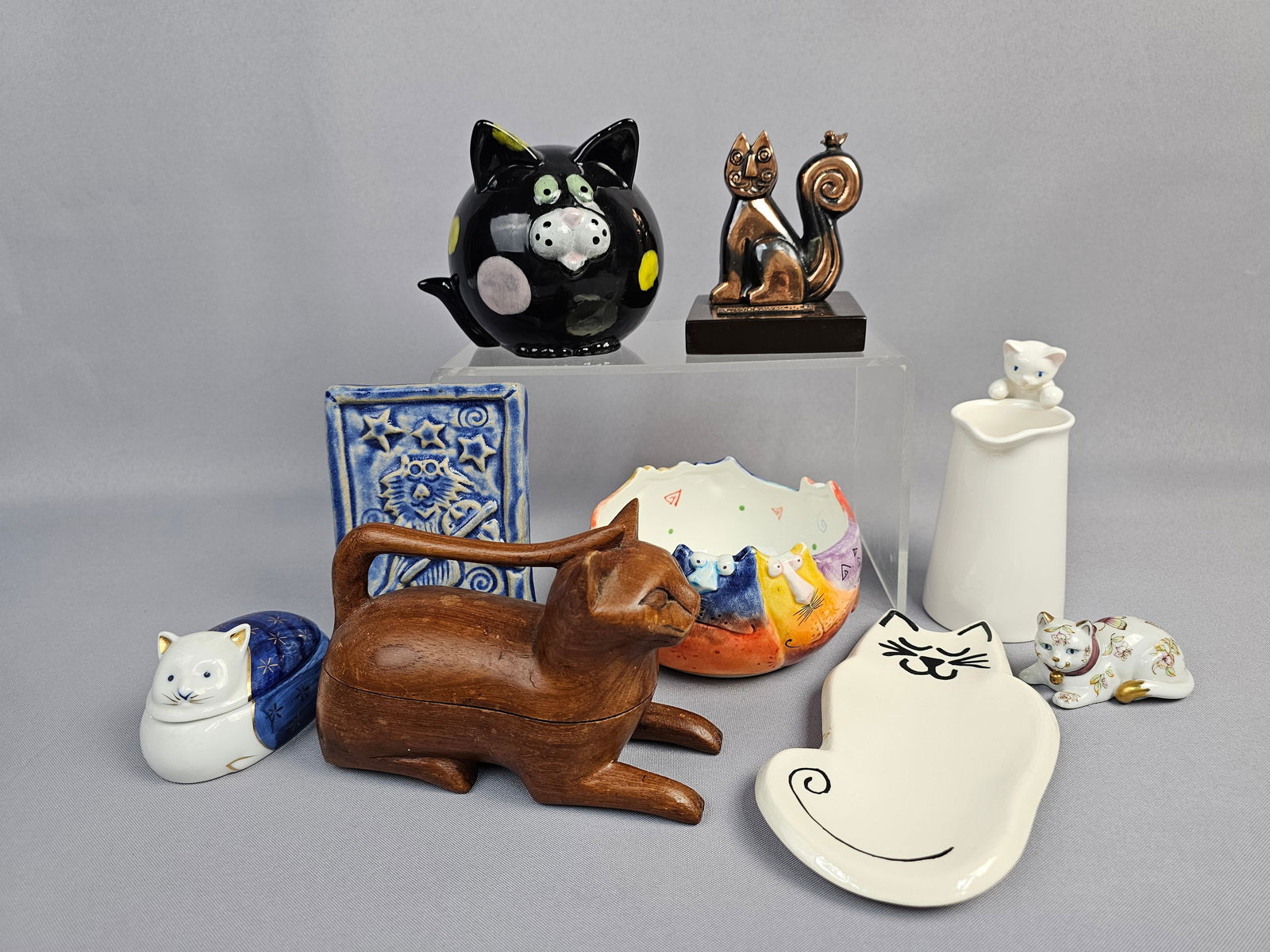A Collection of 9 Assorted Cat-Themed Decorative Objects: A collection of nine decorative objects featuring cat motifs, primarily dating from the late 20th to early 21st centuries and executed in ceramic, wood, and metal. The collection includes several mark