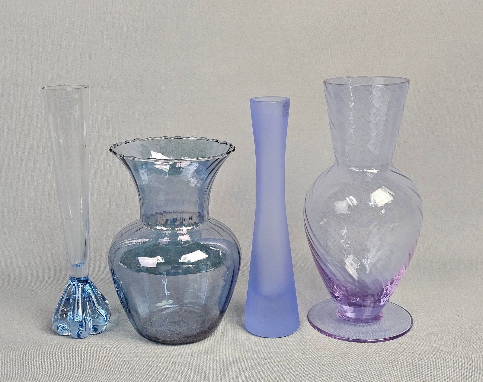 A Collection of 4 Contemporary Art Glass Vases including Teleflora and Polish Examples: The collection consists of four assorted contemporary art glass vases, predominantly featuring a cool color palette of blues, lavenders, and purples. Heights range from 6.5-8.5 inches tall. Generall
