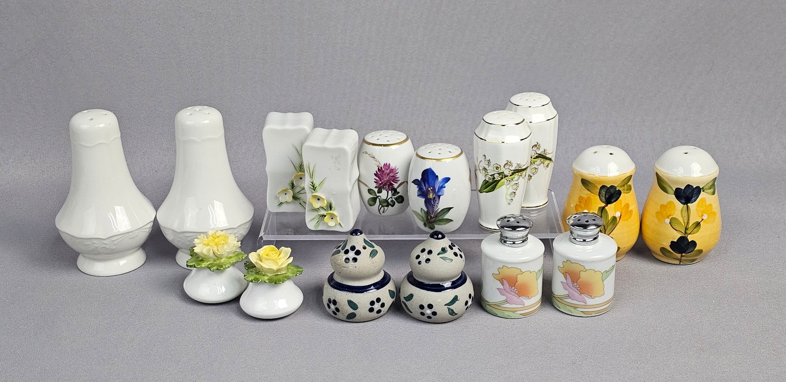 A Collection of 16 Assorted Ceramic and Bone China Salt and Pepper Shakers (Eight Pairs): A collection of 16 individual salt and pepper shakers, comprising eight distinct pairs, predominantly crafted from glazed ceramic and bone china. The collection features a variety of forms and decorat