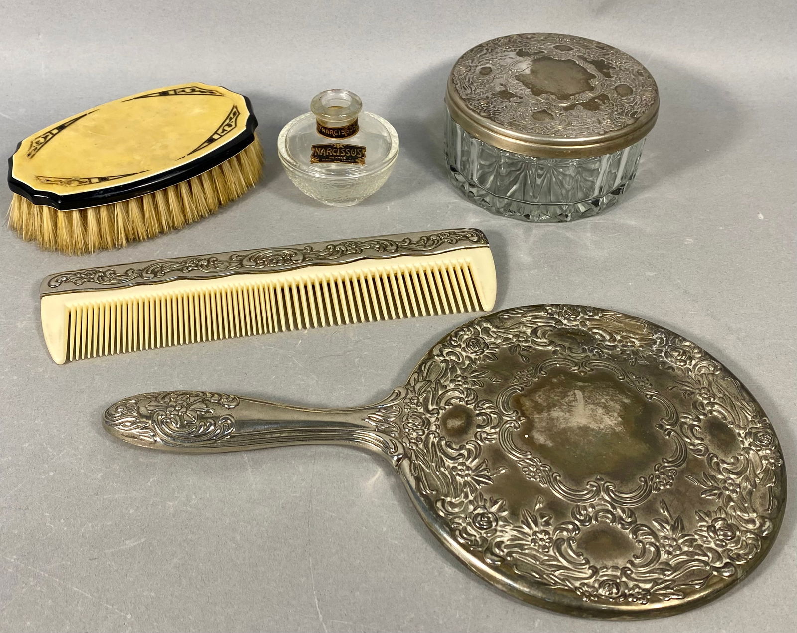 A Collection of Five Vintage Silver-Plated Vanity Items, Early 20th Century: A collection of five vanity items featuring heavy repoussé silver-plated metalwork in a highly ornamented floral or Rococo style. The group includes a handled hand mirror and a hair comb, both
