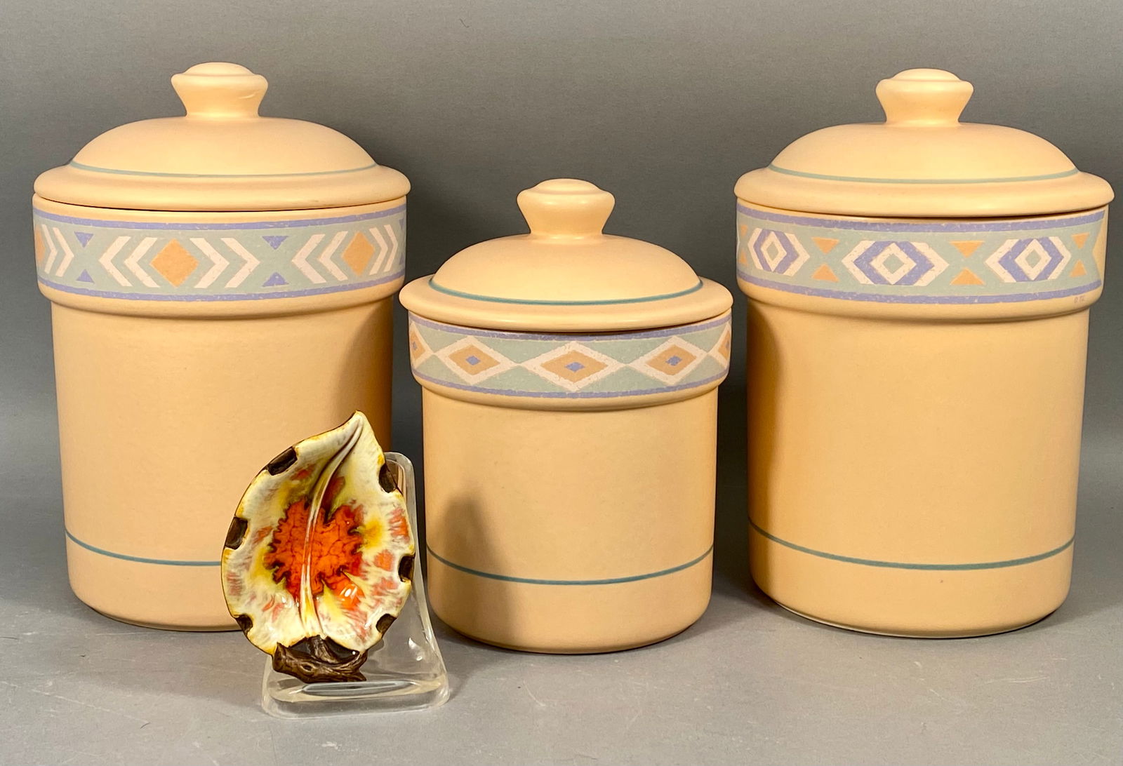 A Collection of Treasure Craft Southwest Peach Canisters and 1962 Leaf Dish: A collection of ceramic items by Treasure Craft, featuring three lidded canisters in the Southwestern or Aztec pattern, along with one decorative leaf-shaped dish. The canisters are constructed of mat
