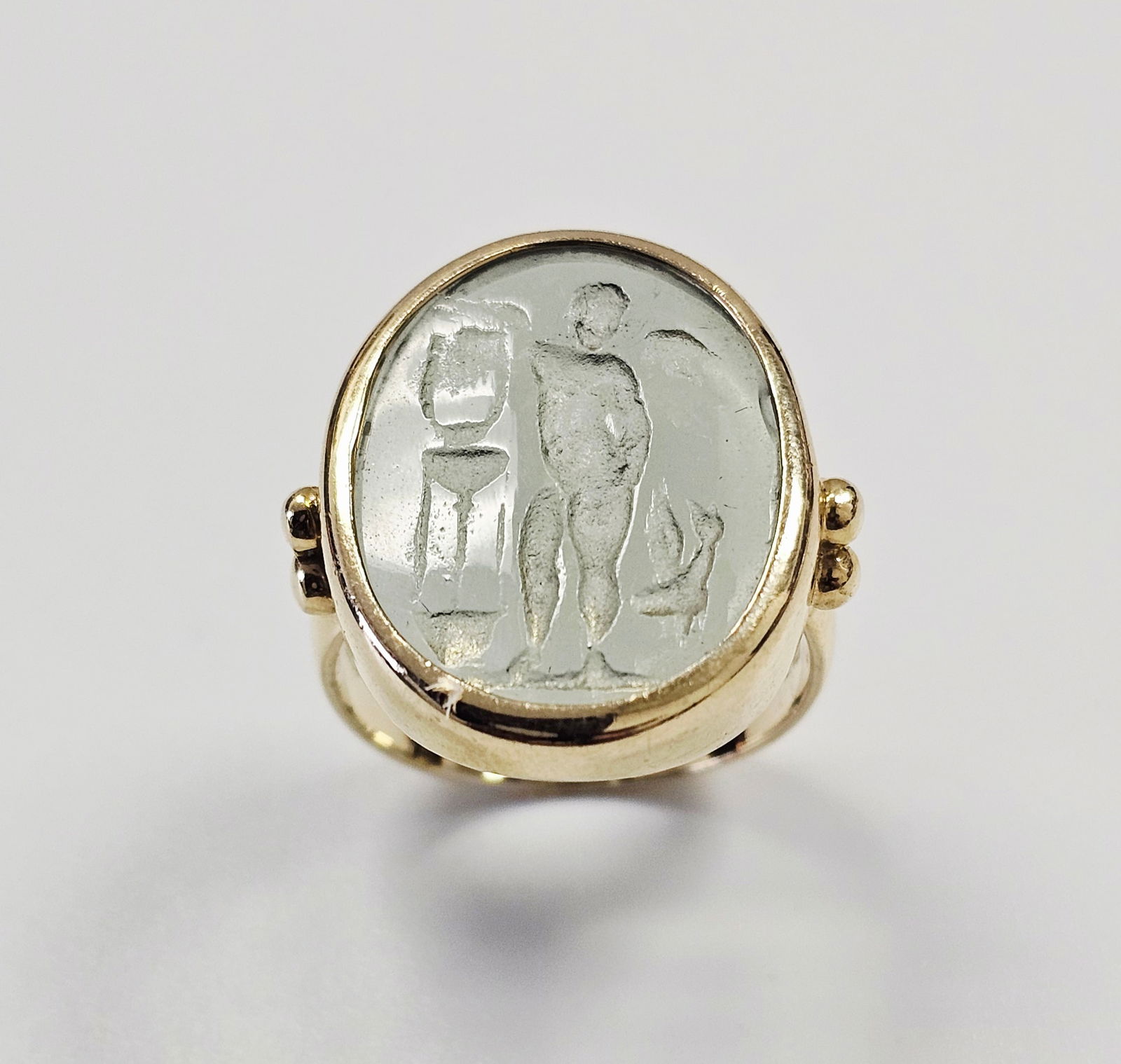 A 14kt Yellow Gold and Pale Green Intaglio Ring: This 14kt yellow gold ring features an oval, bezel-set intaglio carved into a translucent, pale green-tinted gemstone, likely rock crystal or glass. The classical-style intaglio depicts a standing nud