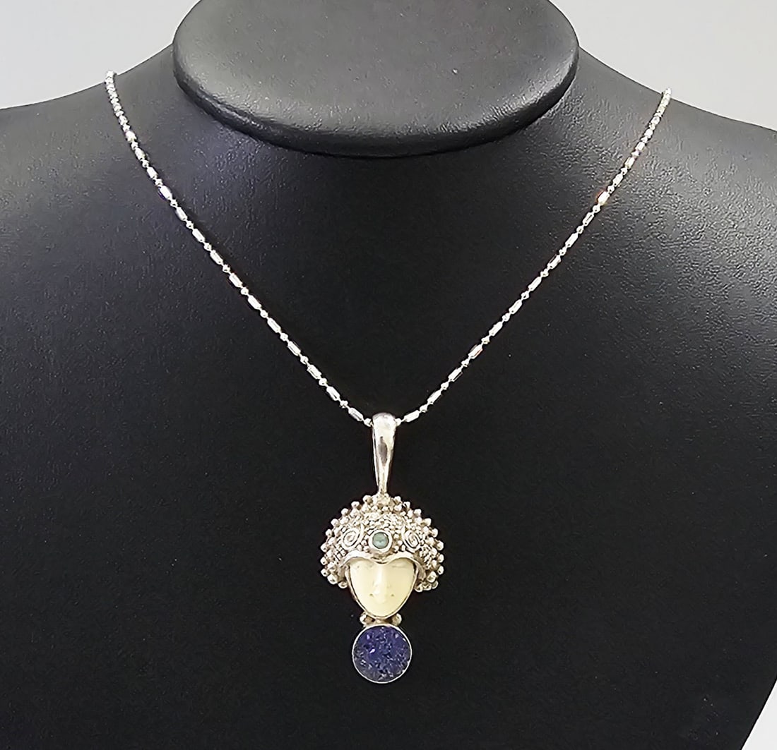 Sajen Sterling Silver Carved Goddess Pendant with Lapis Druzy and Blue Topaz Necklace: A Sajen sterling silver pendant necklace featuring a hand-carved goddess face. The face is carved from bone and set within an ornate sterling silver headdress. The headdress is decorated with traditio