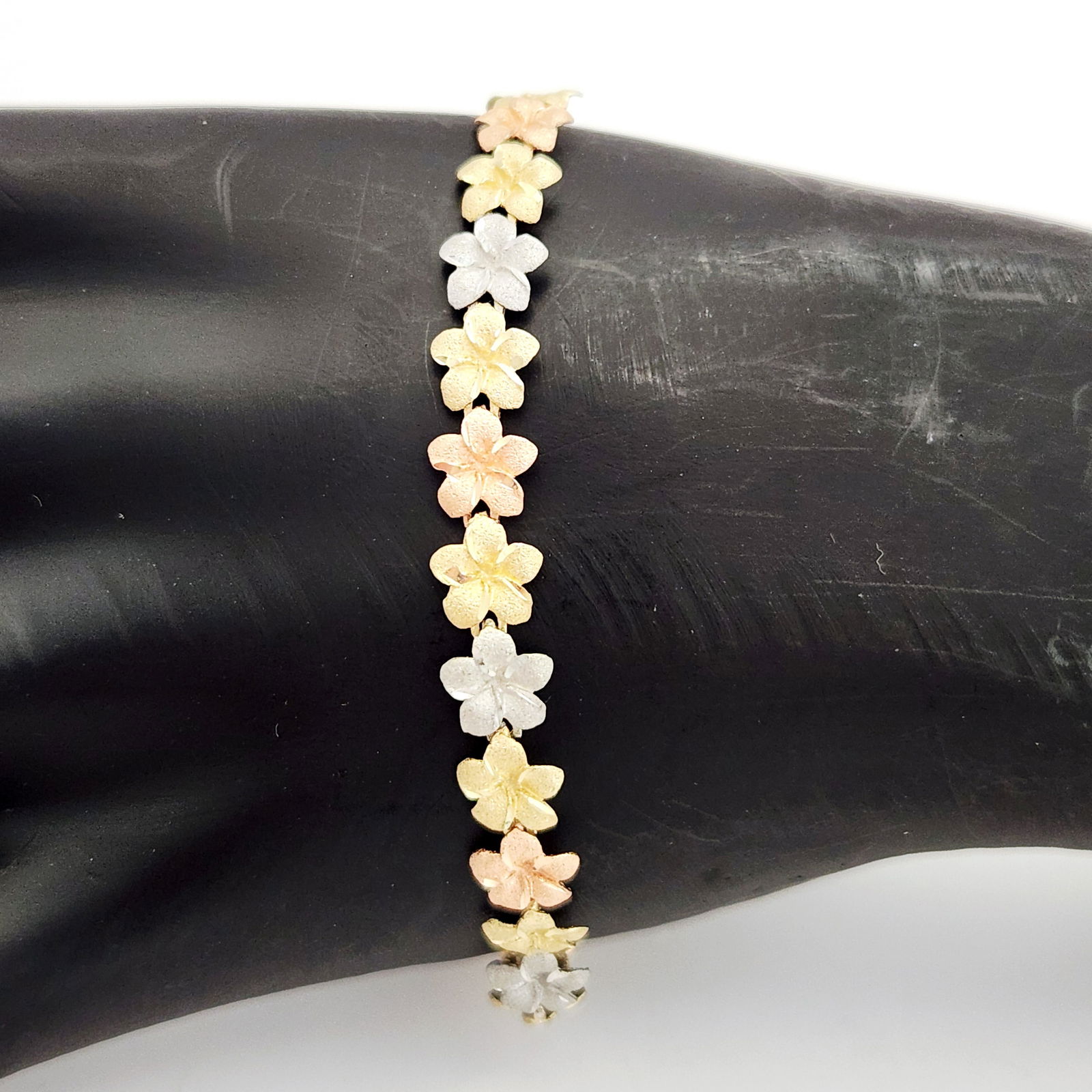 14K Tri-Gold Bracelet 7 Grams: This tri-color 14K gold link bracelet features a repeating sequence of textured plumeria blossoms in alternating yellow, rose, and white gold. Each five-petal flower link is finished with a sand-blast