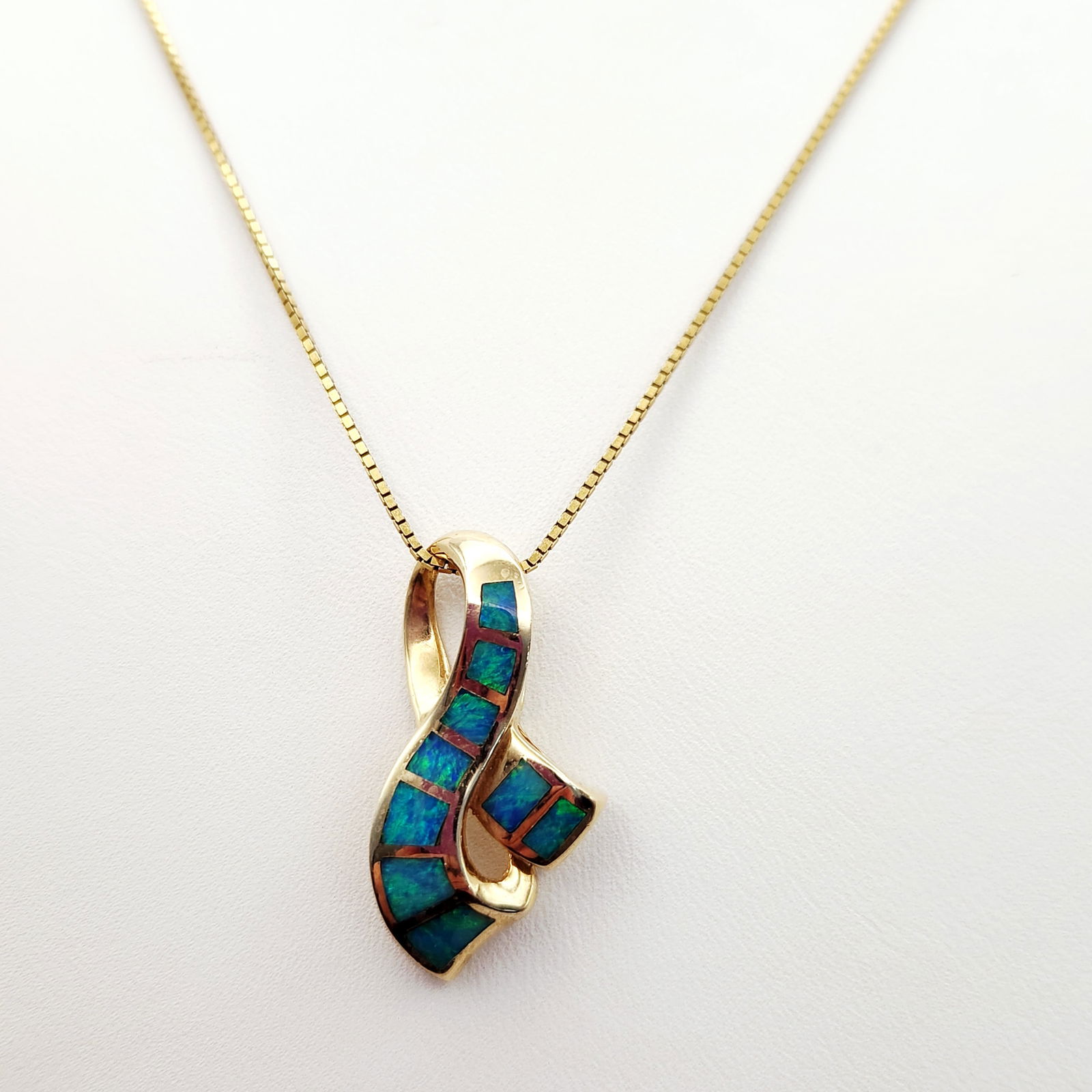 14K Gold Opal Pendant Necklace 9.6 Grams: A 14K yellow gold necklace featuring a modern, abstract ribbon-style pendant. The pendant is decorated with channel-set rectangular segments of blue and green inlay opal. The reverse of the pendant di