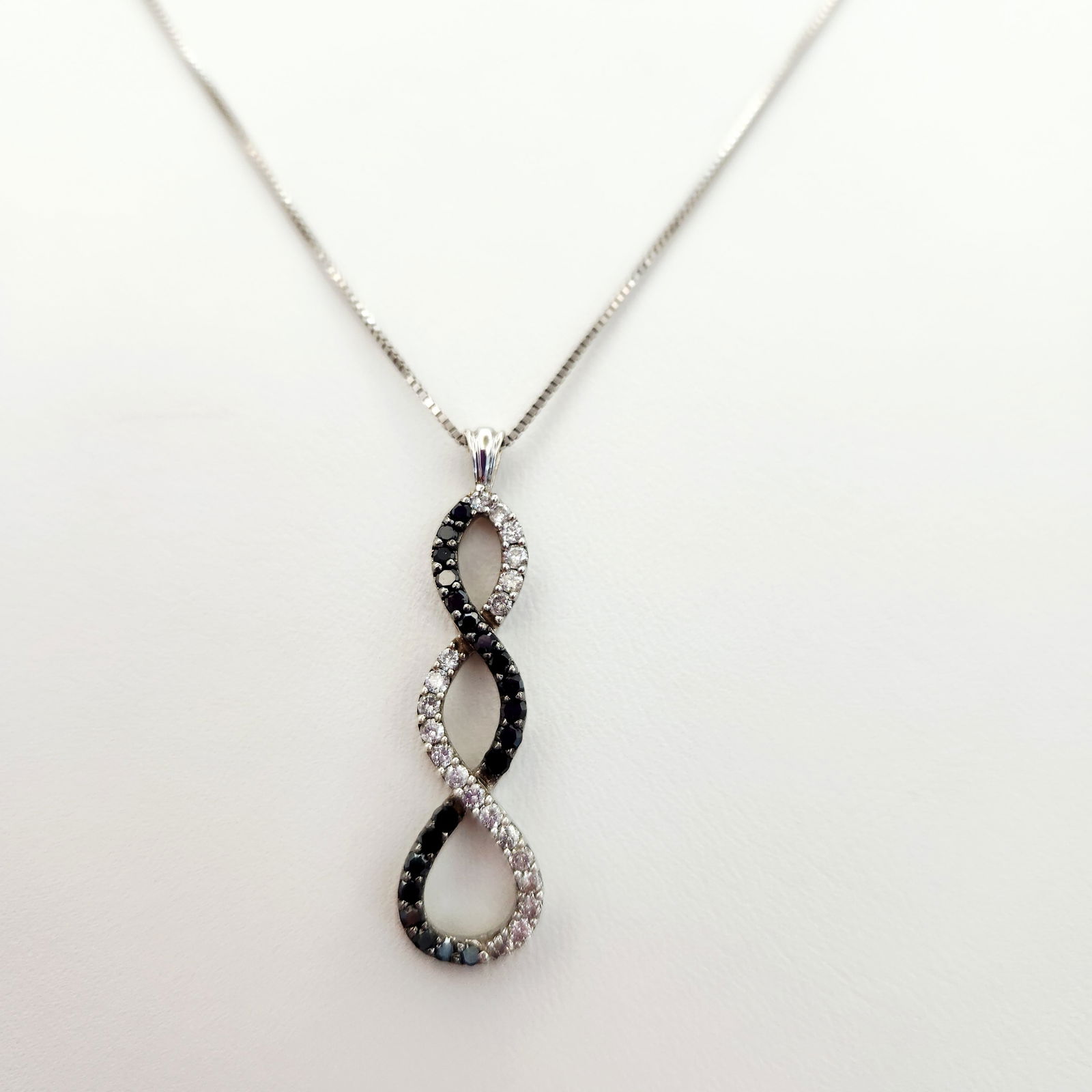 10K Gold Diamond Pendant Necklace 4 Grams: A 10-karat white gold necklace featuring a pendant designed as three interlocking infinity loops. The pendant is pavé-set with alternating sections of small round white and black accent diamond