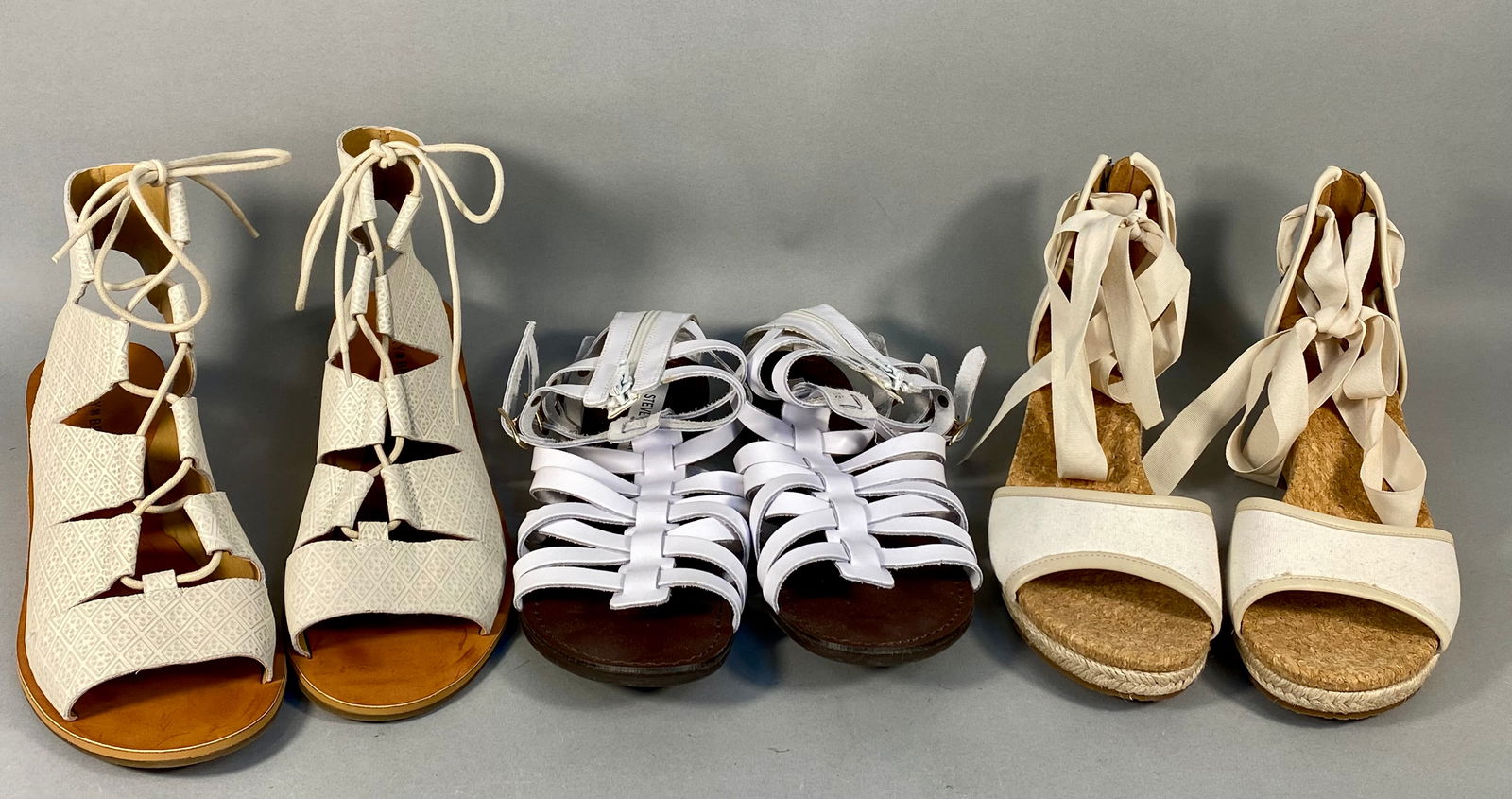 A Trio of Women's Sandals by Lucky Brand, Steve Madden, and UGG: A collection of three pairs of women's sandals in neutral cream and white tones. The first pair consists of Lucky Brand Gizi lace-up wedge sandals featuring leather uppers with an embossed geometric p