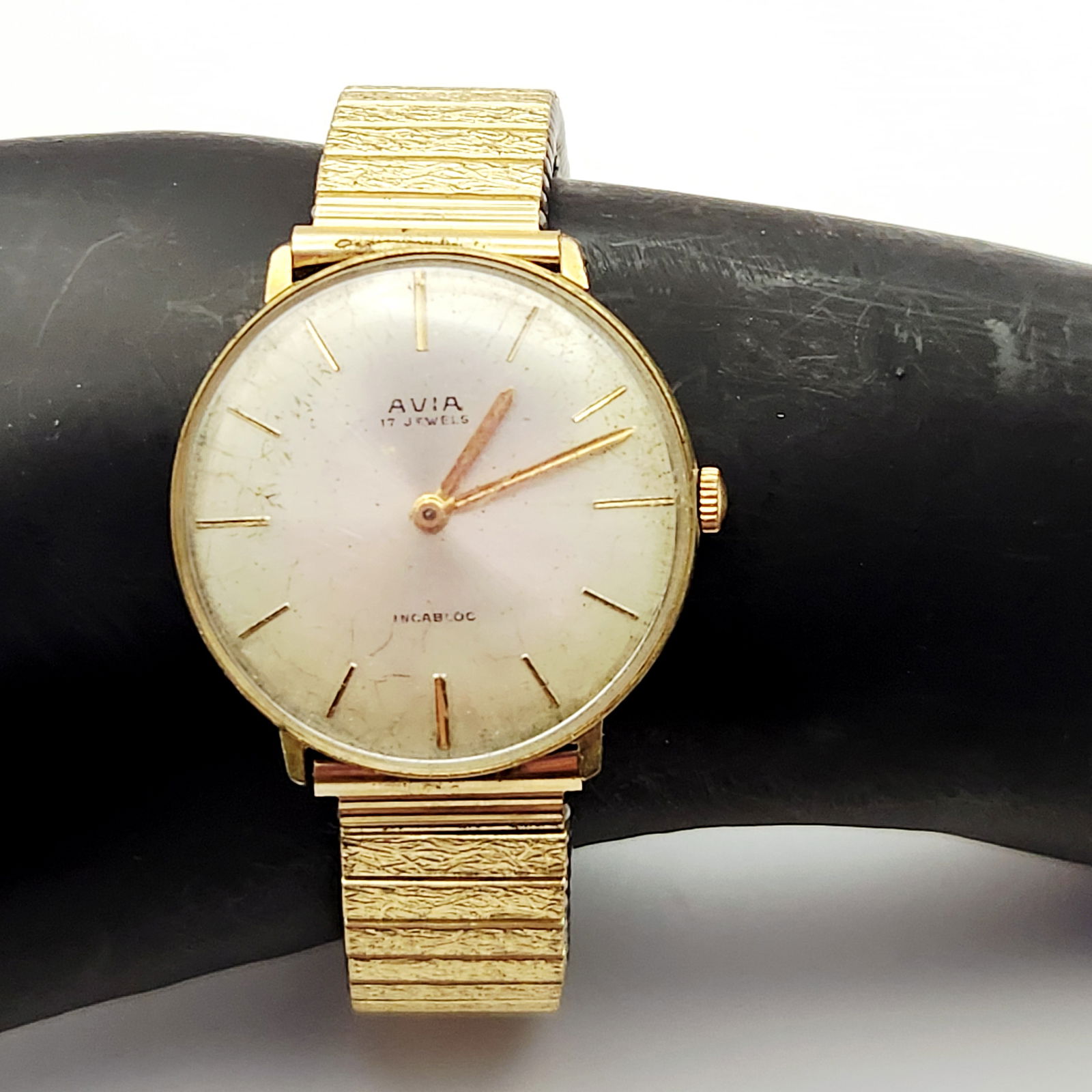 Avia 17 Jewels Incabloc Gold Toned Wristwatch: A gold-toned Avia wristwatch featuring a silver-colored face, stainless steel back, and a rolled gold Fixo-Flex expansion band, weighing 59.8g. The crystal is scratched and the face is marked, see pi