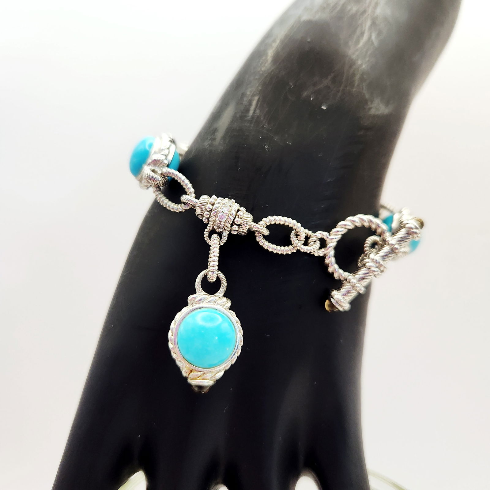 Judith Ripka Sterling Bracelet 34 Grams: This Judith Ripka sterling cable-link charm bracelet features several turquoise-colored round cabochons set in decorative rope-textured bezels. The piece is secured with a toggle clasp accented by sma