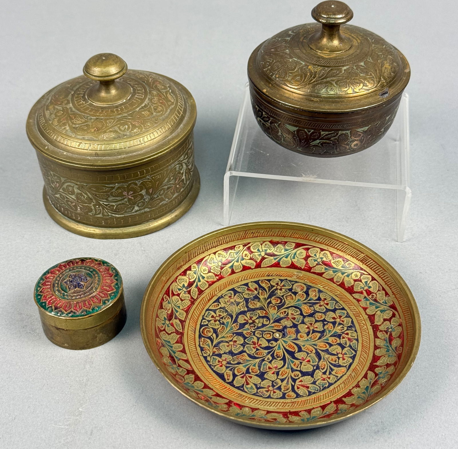 A Collection of Four Enameled and Engraved Brass Decorative Items: A collection of four decorative items crafted from brass or bronze, likely exhibiting a Middle Eastern or Indian style. The collection includes two lidded containers, one cylindrical and one hemispher