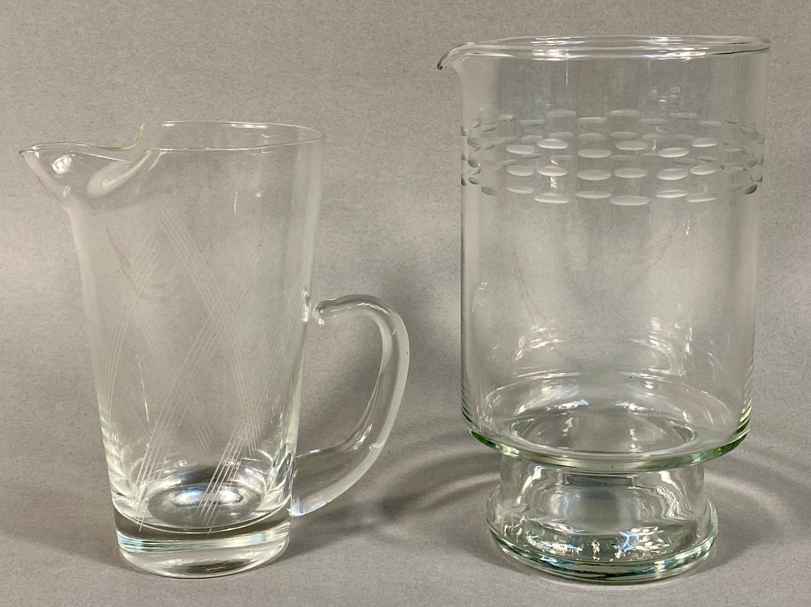 A Vintage Etched Glass Pitcher and Cocktail Mixer: A pair of clear colorless glass serving vessels consistent with Mid-Century Modern design. The first item is a handled beverage server featuring a flared rim, wide pouring spout, and applied handle. I