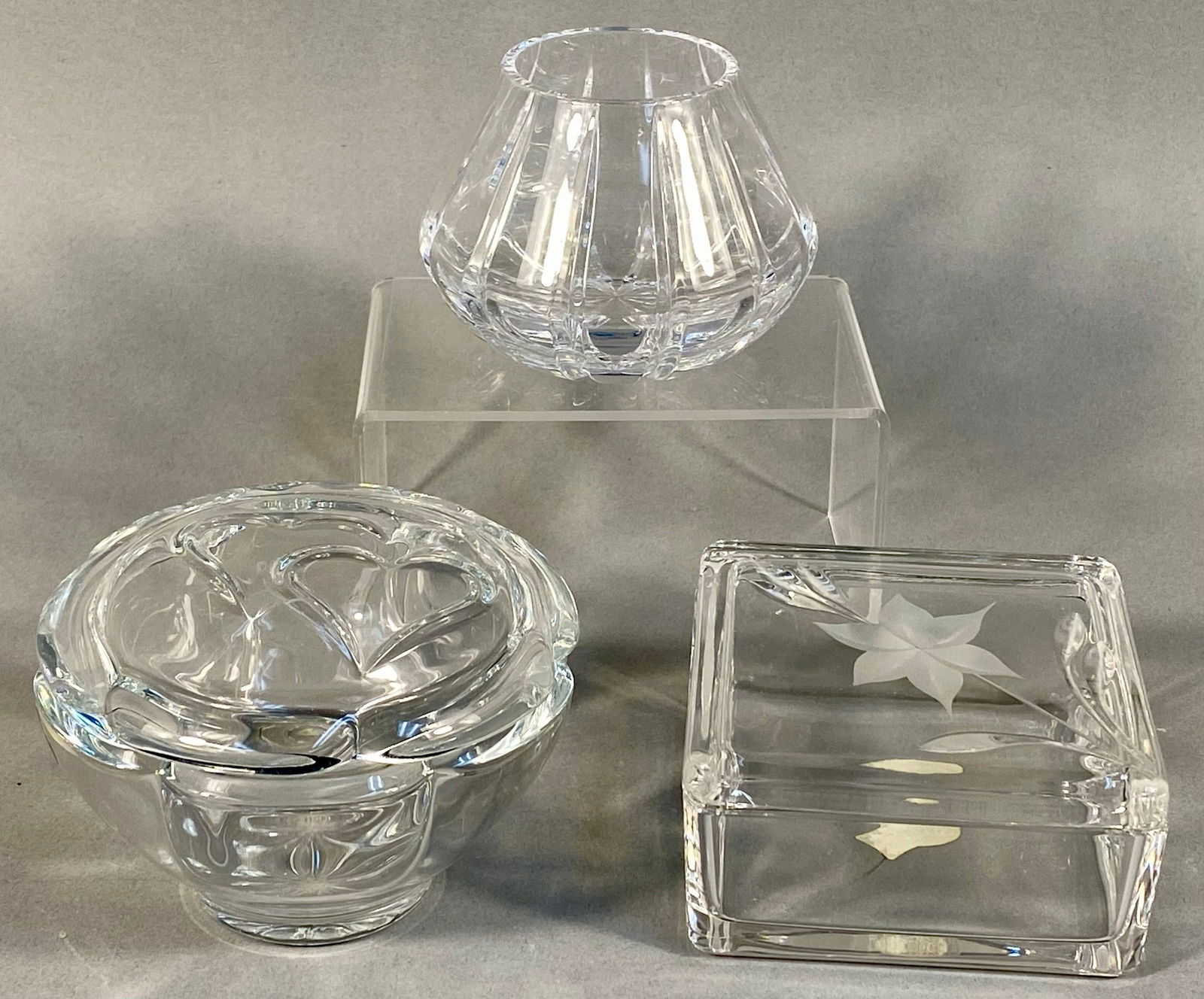 A Trio of Lead Crystal Decorative Items, Including RCR Royal Crystal Rock: A collection of three clear, highly faceted lead crystal decorative objects. The lot comprises one small, vertically cut vase or votive holder; one round lidded dish featuring molded double-heart desi