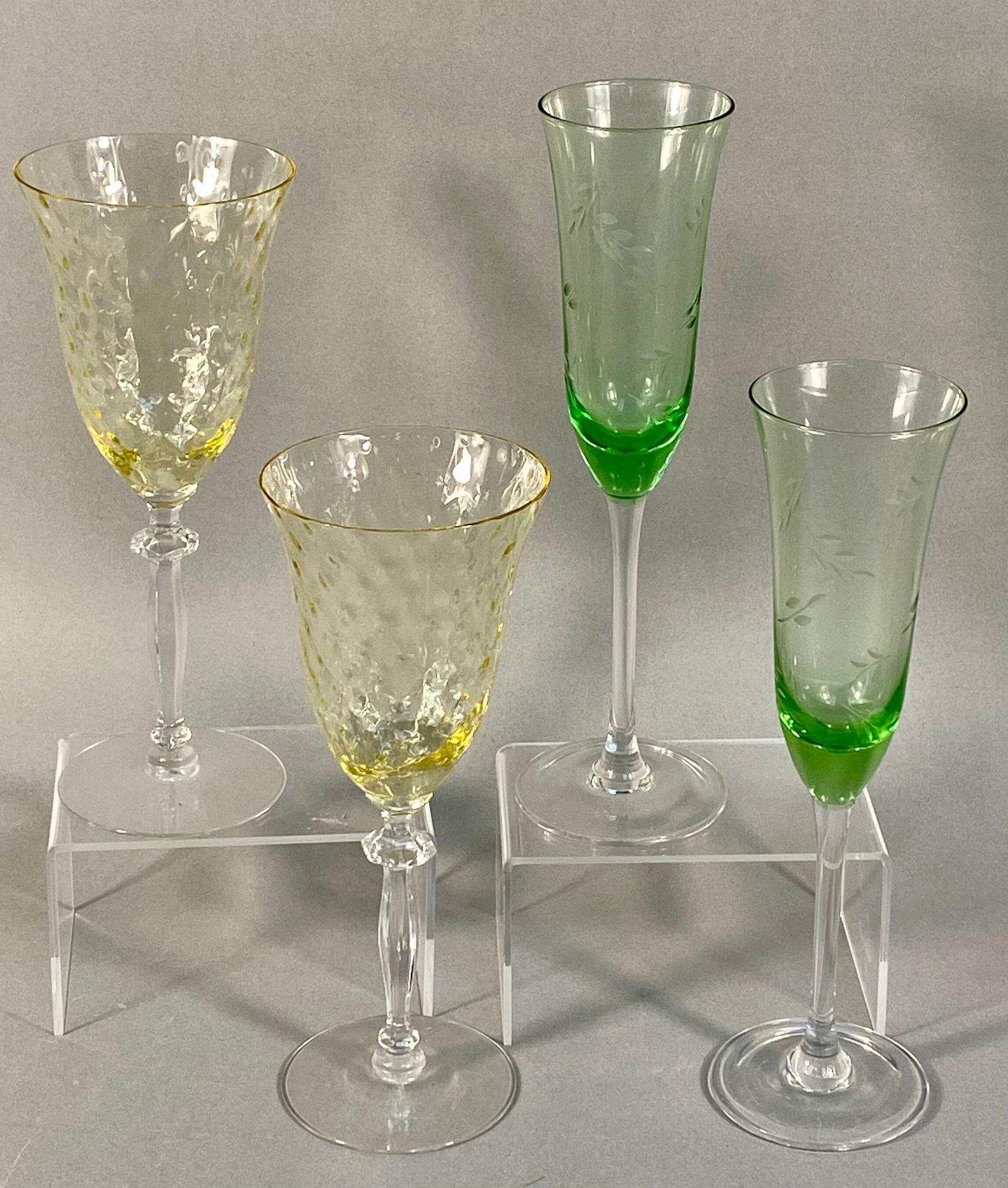 A Collection of Four Vintage Glass Stemware Items: A collection of four stemmed drinking glasses possibly constructed of uranium glass, presented as two distinct pairs. The first pair consists of two goblets featuring a pale yellow bowl decorated with